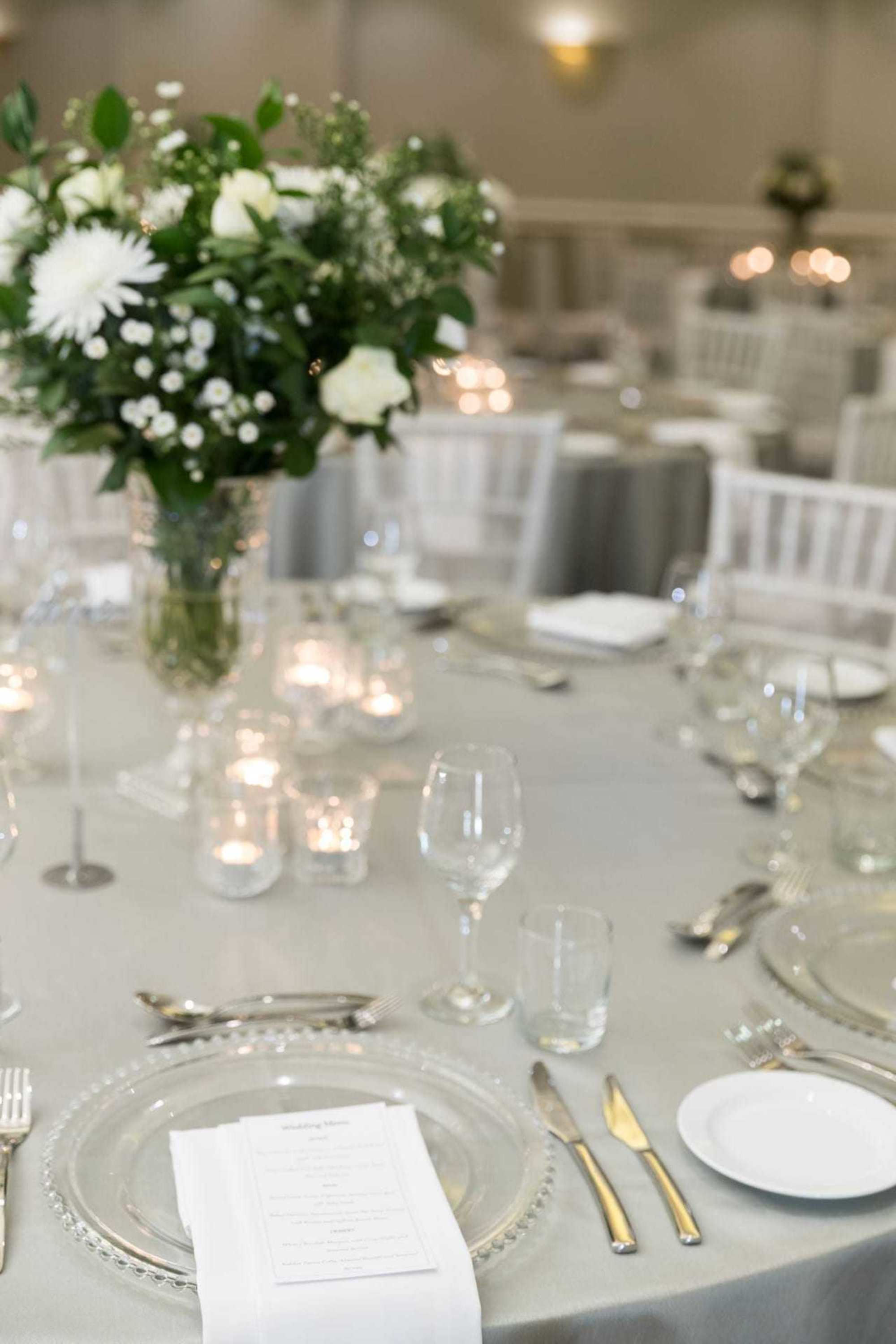 Elegant wedding reception table with white floral centerpiece, candlelight, and neatly arranged glass and silverware.