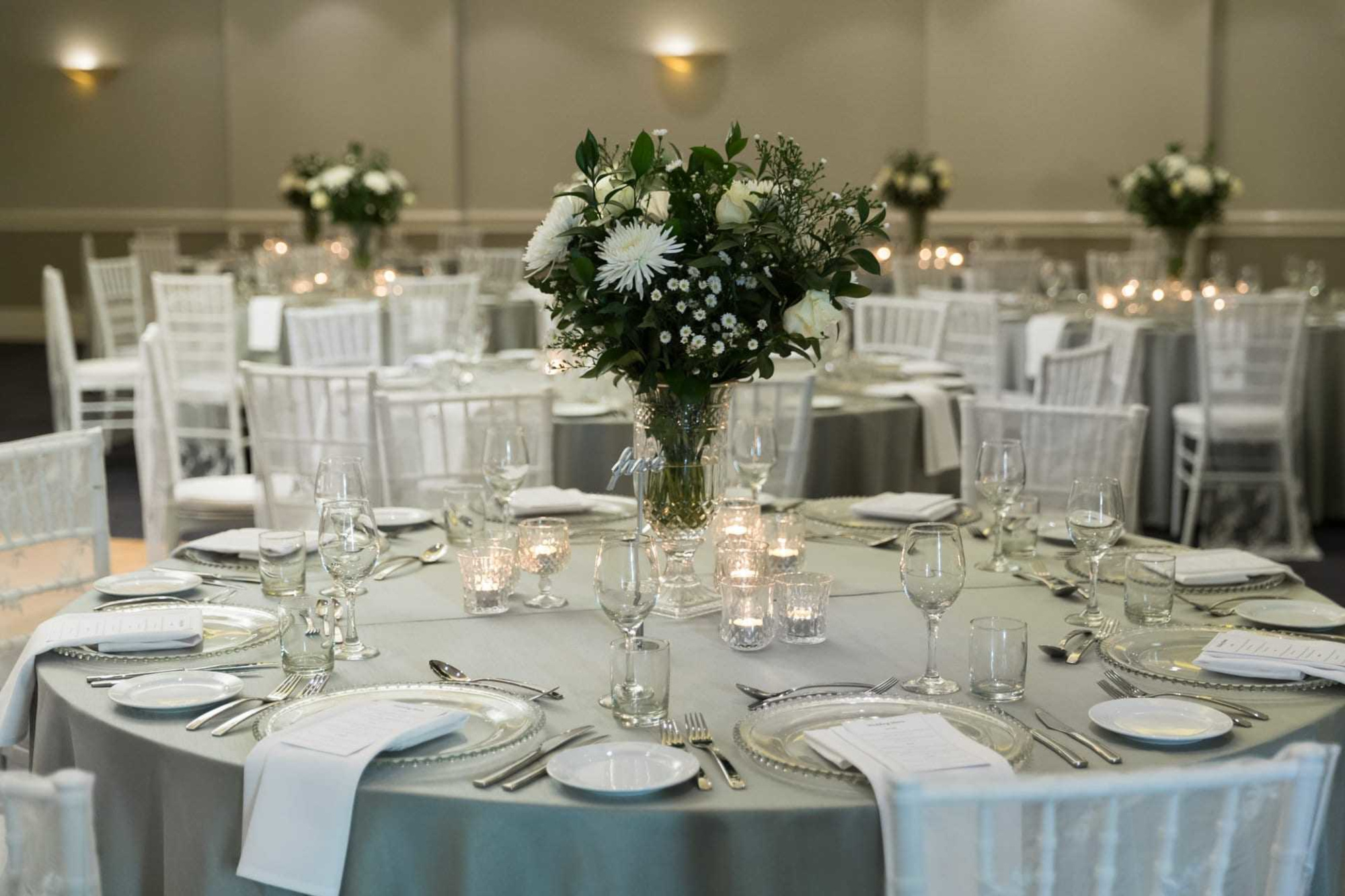 Elegant indoor wedding reception with round tables, white floral centerpieces, and candlelit place settings.