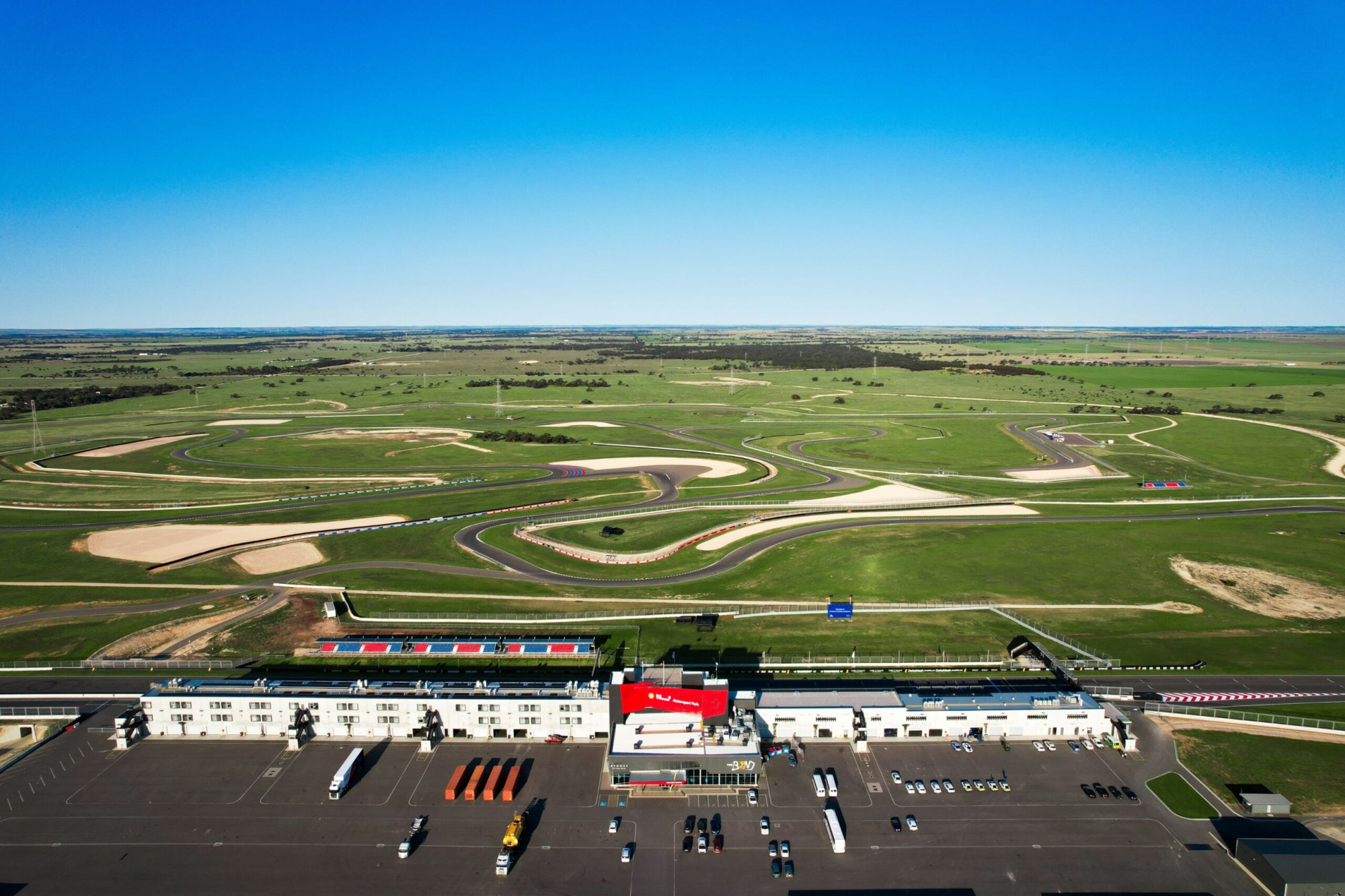 Aerial view of a sprawling racetrack complex surrounded by open green fields under a clear blue sky.
