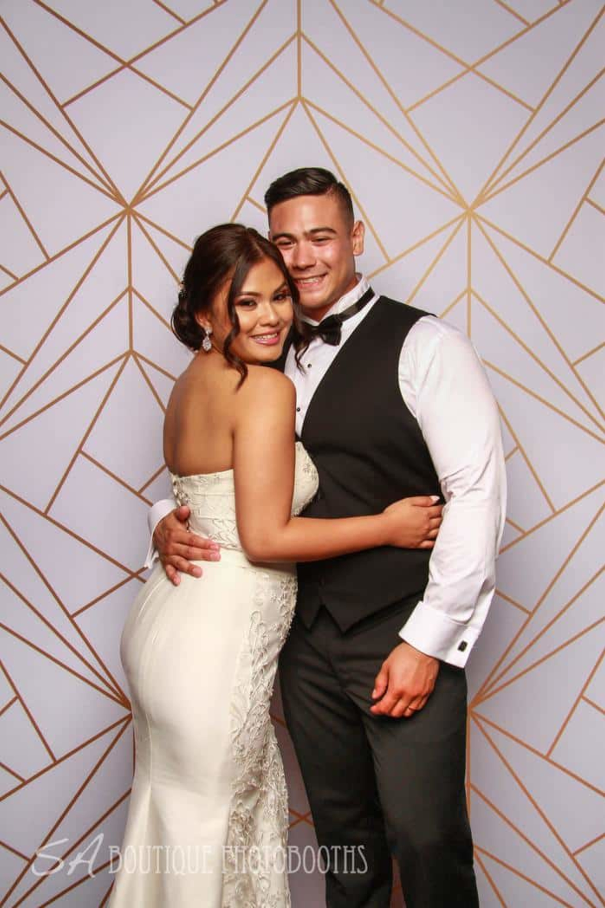 Smiling wedding couple posing in front of a modern geometric photo booth backdrop.