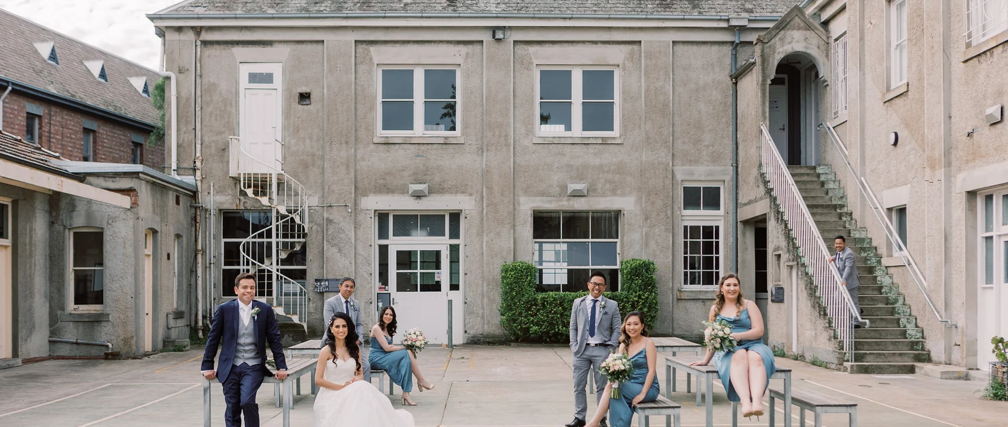 Wedding party posing on benches in a courtyard of a concrete urban building.
