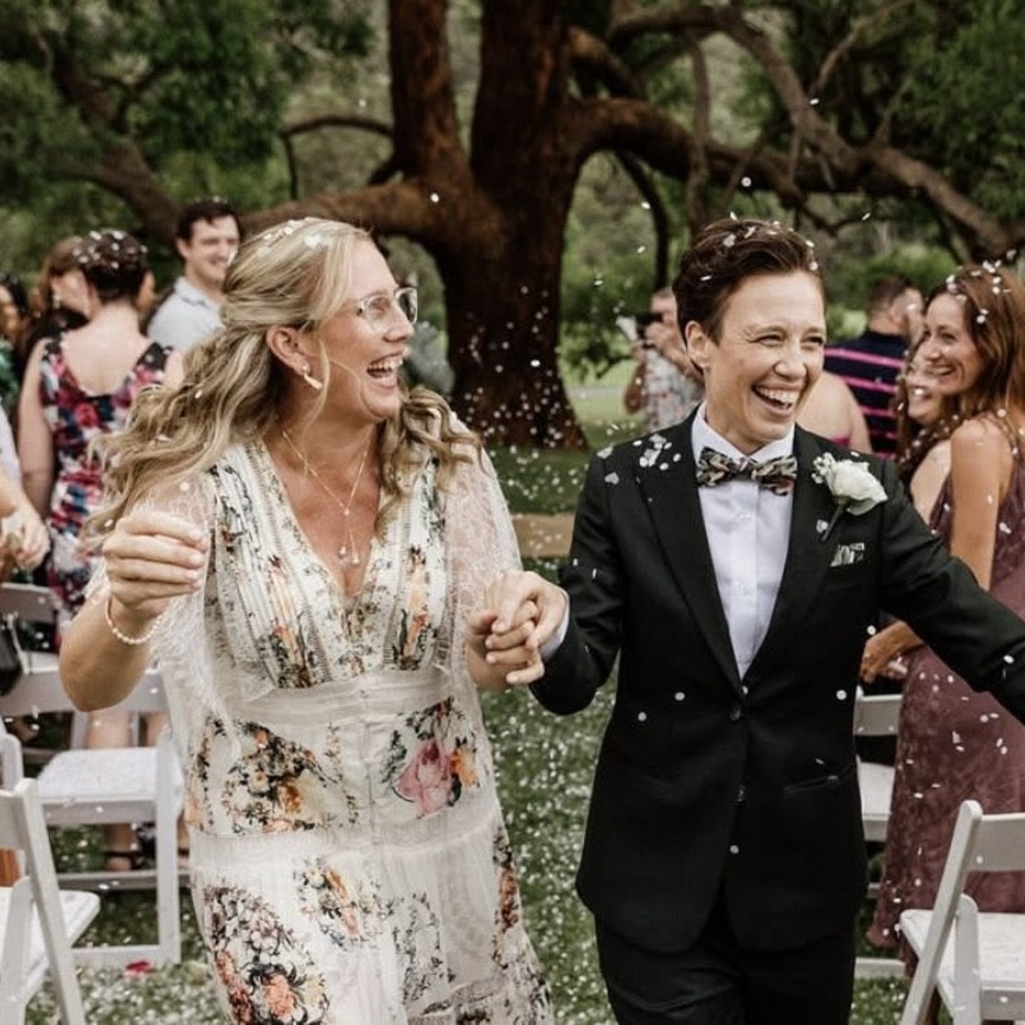 Joyful couple walks through confetti during their outdoor wedding ceremony surrounded by guests.