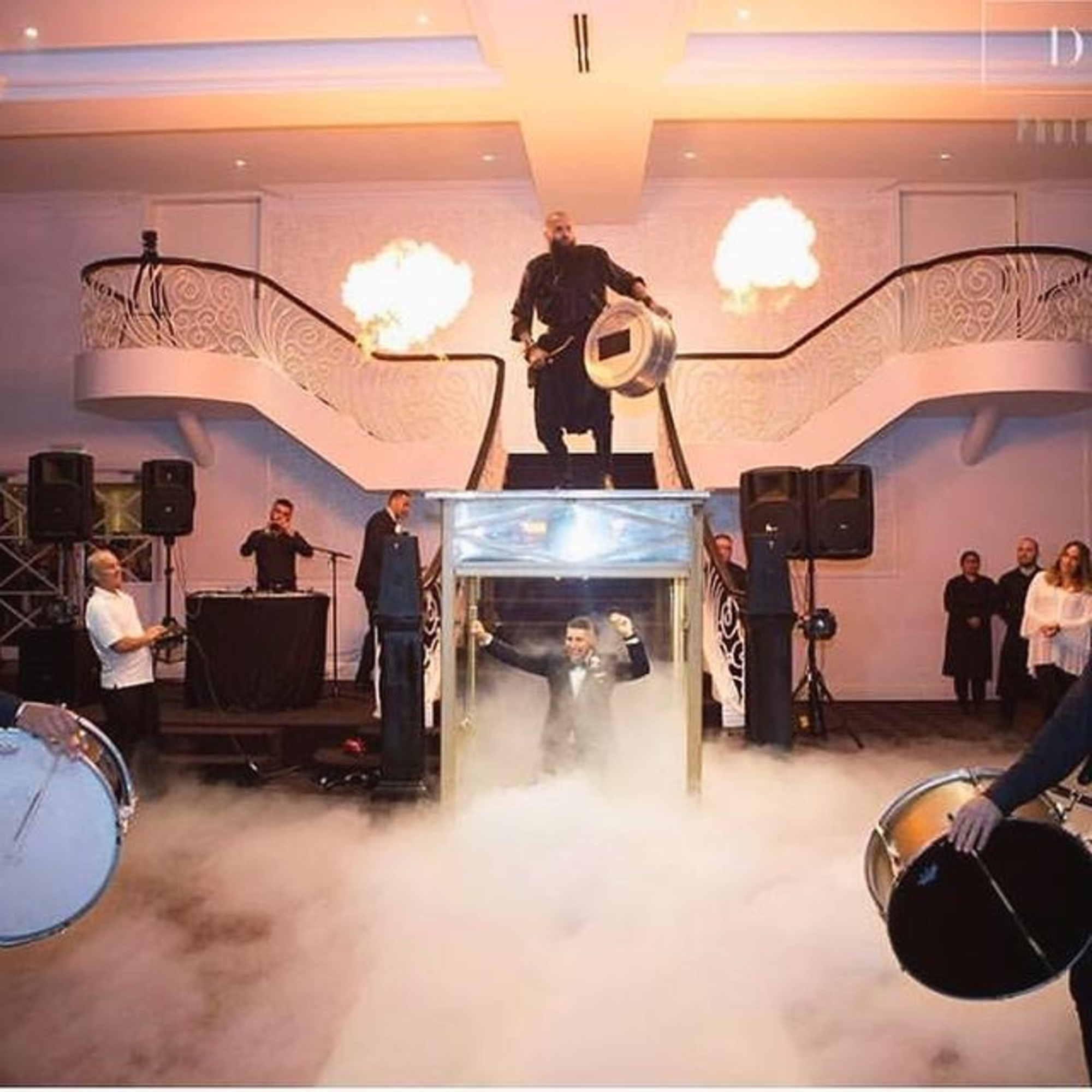 Dramatic wedding reception entrance with groom emerging through fog, drummers, and fire effects on a grand staircase stage.