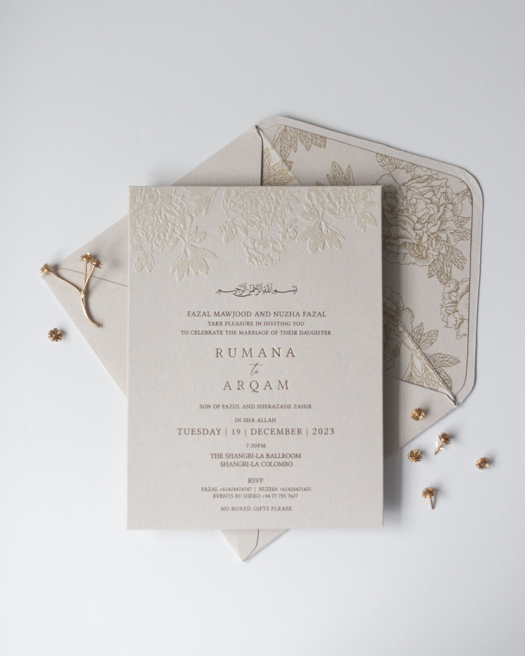 Neutral floral embossed wedding invitation with gold text and matching envelope flat lay.