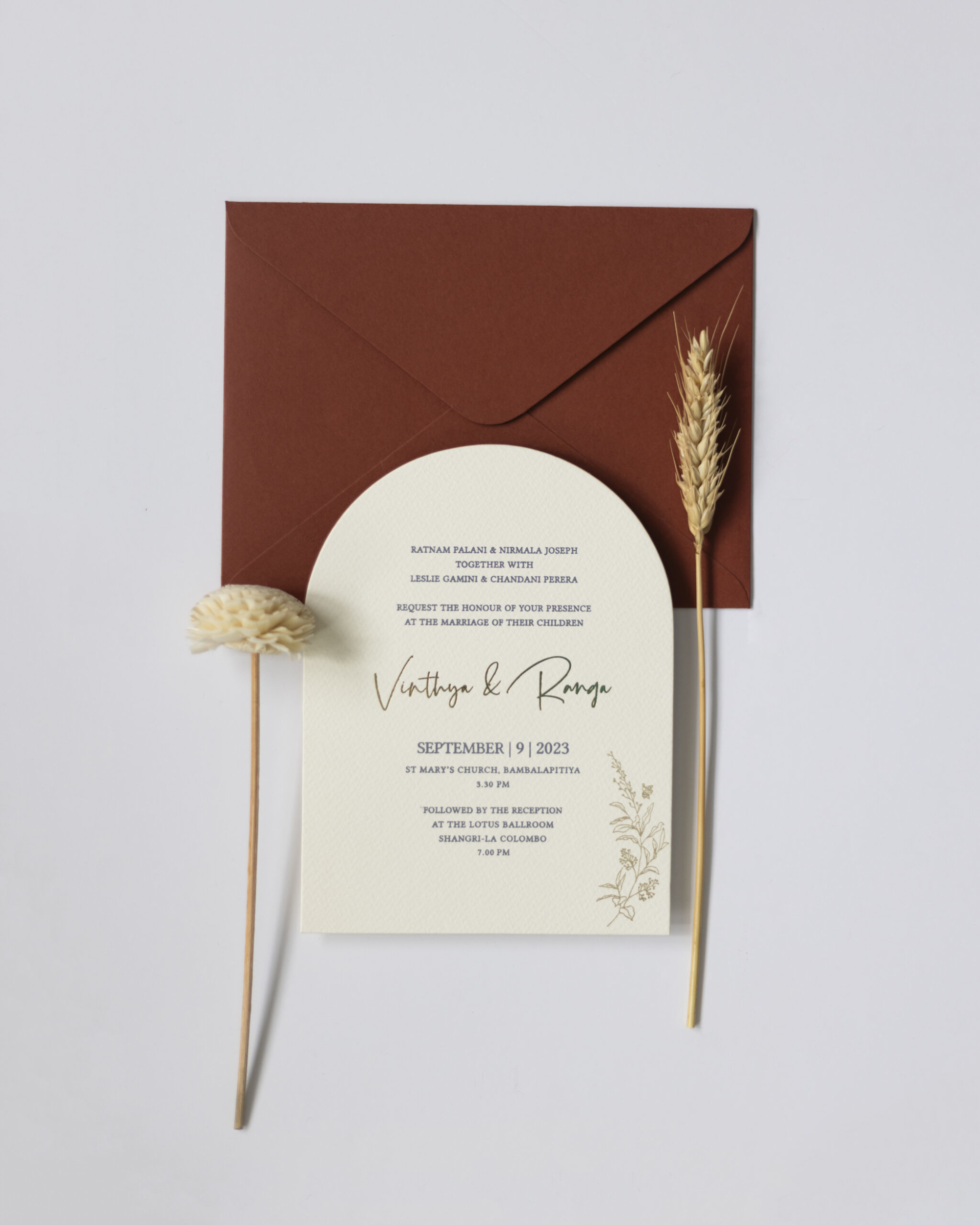 Minimalist wedding invitation with rust envelope and dried floral accents on a light background.