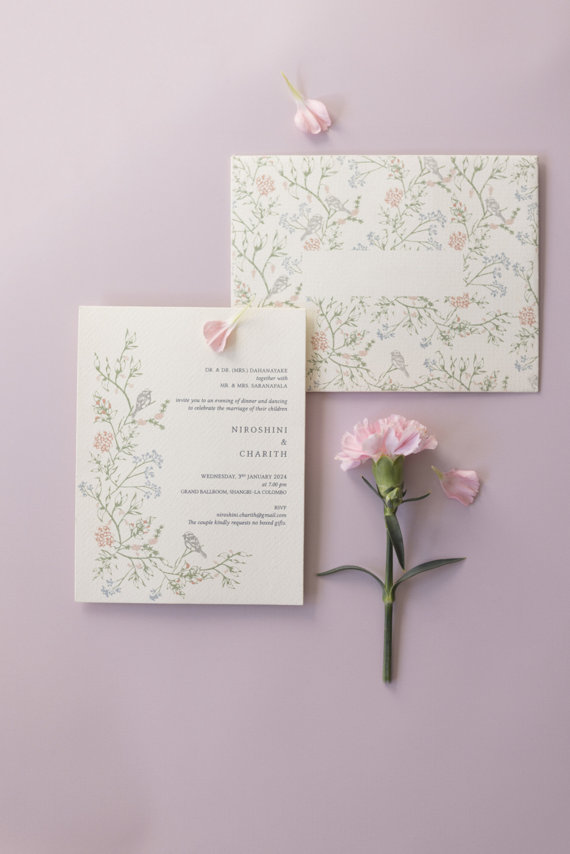 Floral botanical wedding invitations styled on a pastel pink background with pink carnation flowers.