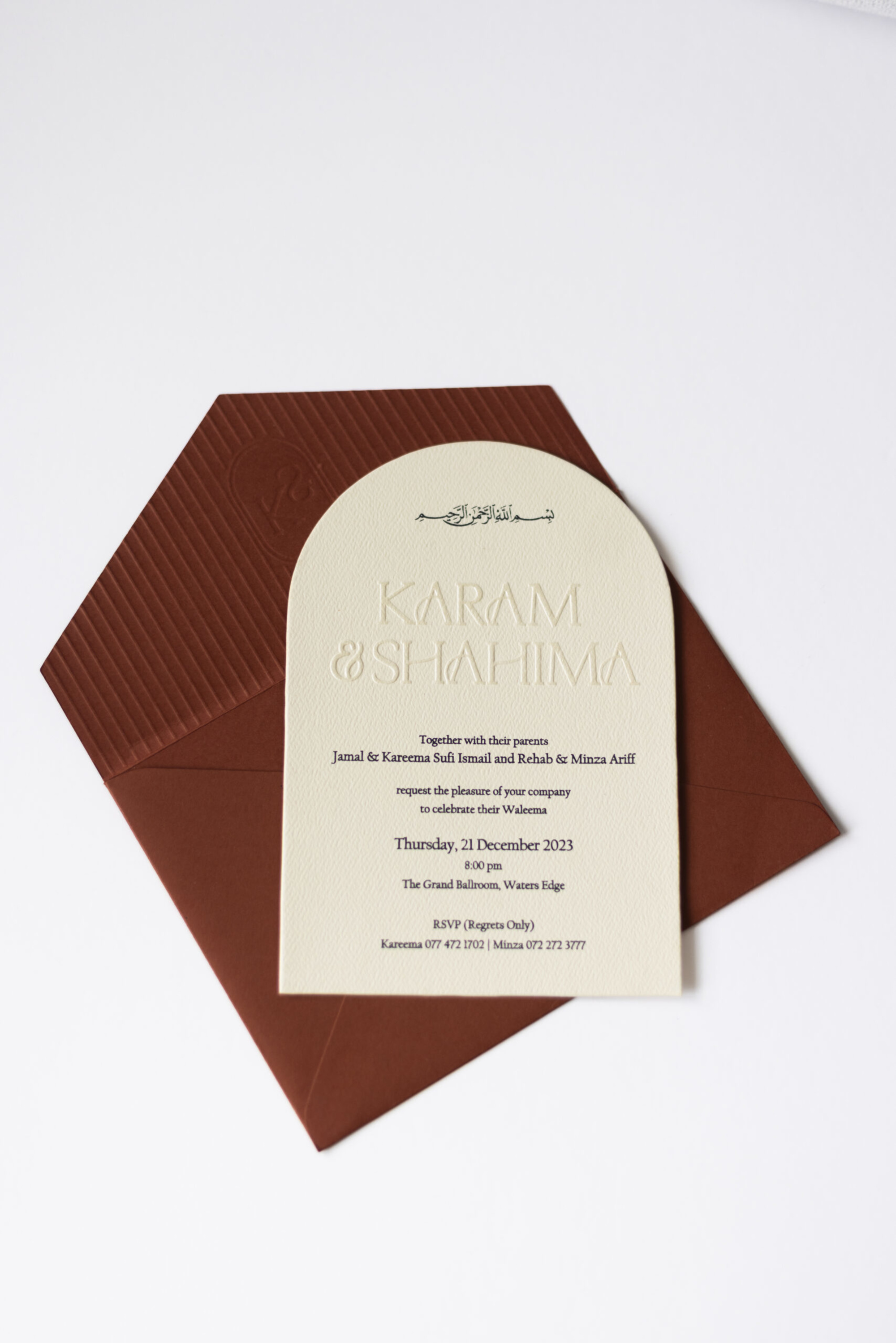 Arched cream wedding invitation card with embossed names on a rust brown envelope against a white background.
