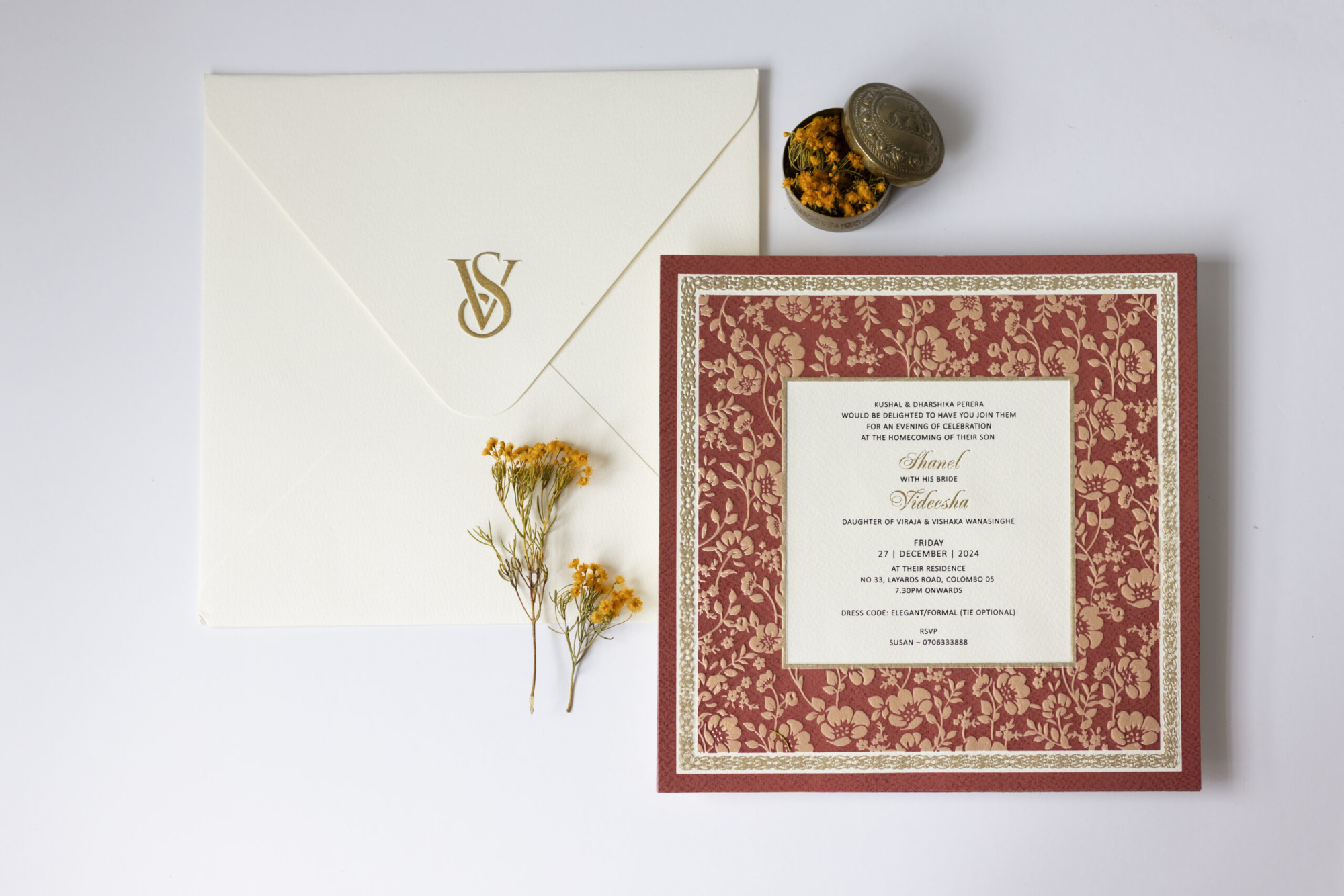 Elegant floral wedding invitation suite with red and cream card, monogrammed envelope, and yellow dried flowers on a white background.