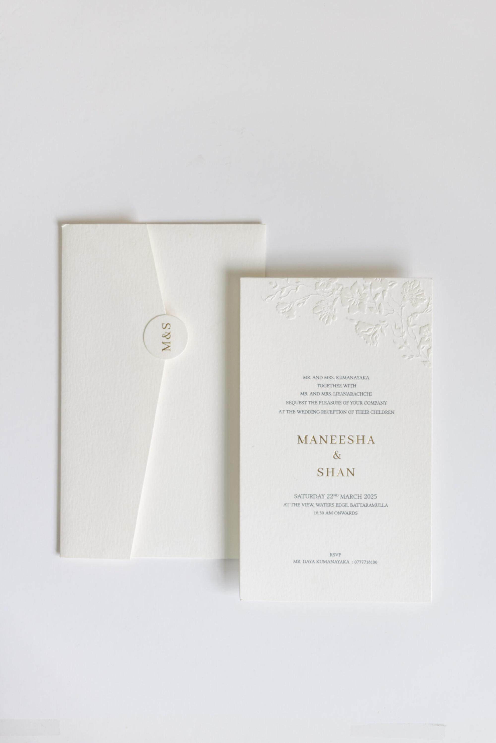 Minimal ivory wedding invitation card with embossed floral detail and matching envelope on a white background
