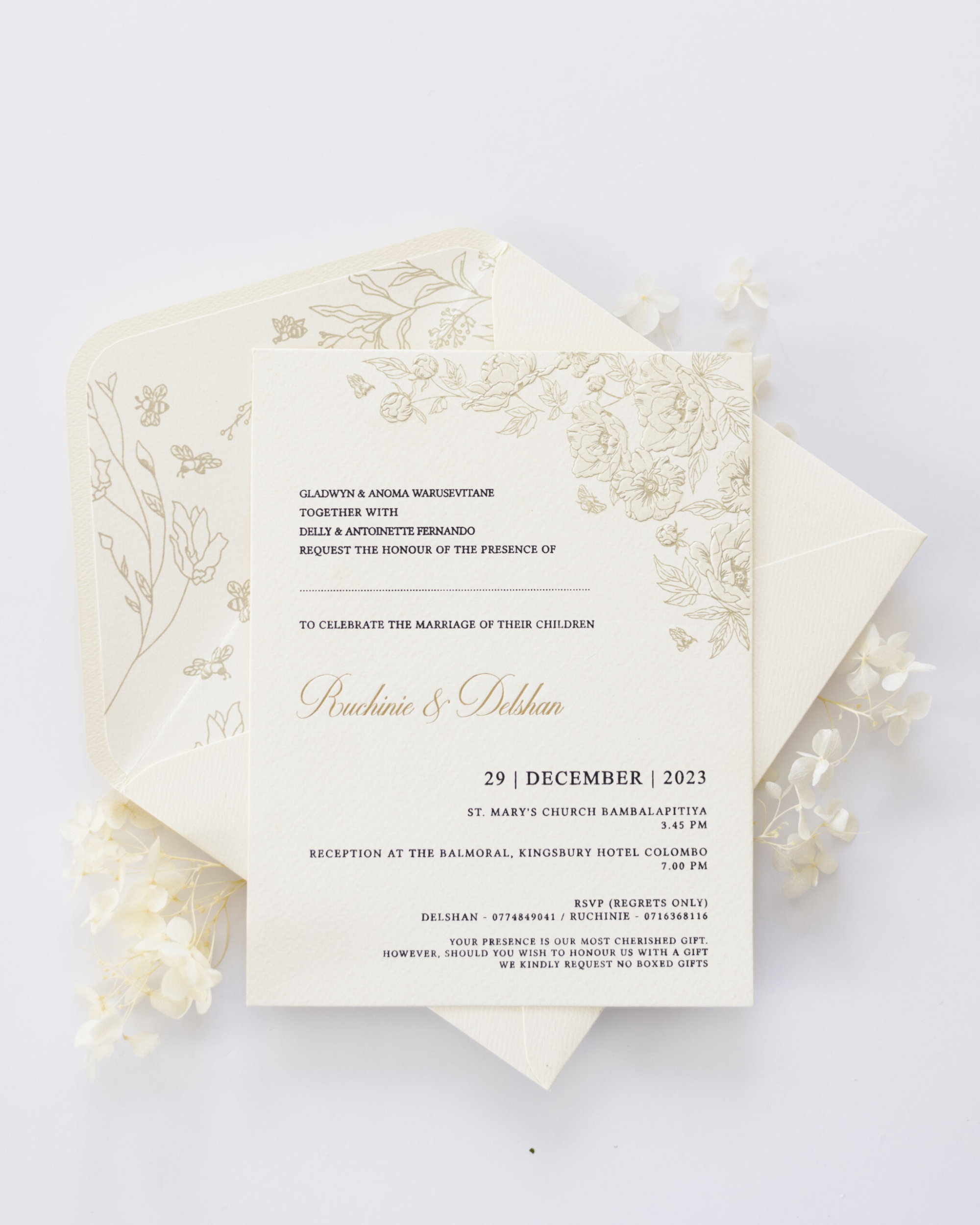 Elegant cream floral wedding invitation suite with scripted names and matching envelope on a light background.