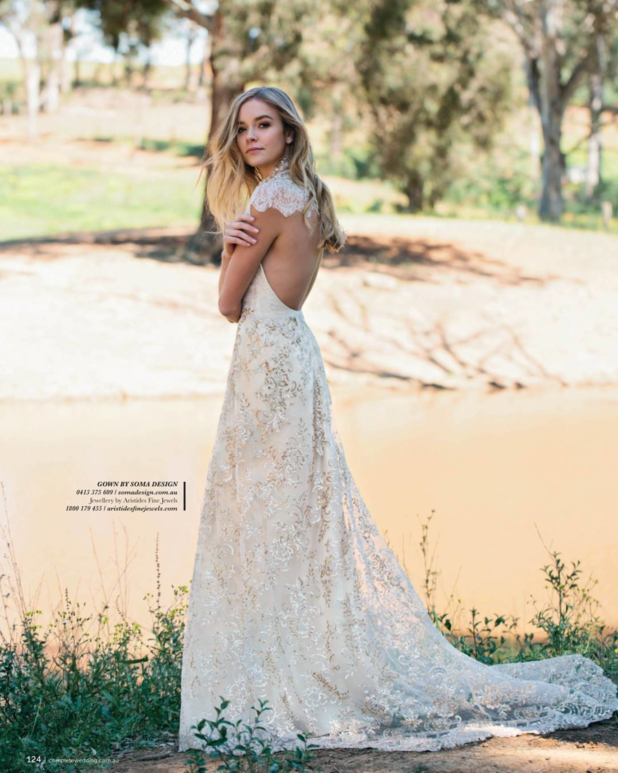 Bride in a lace backless wedding gown standing by a lakeside in a natural outdoor setting.