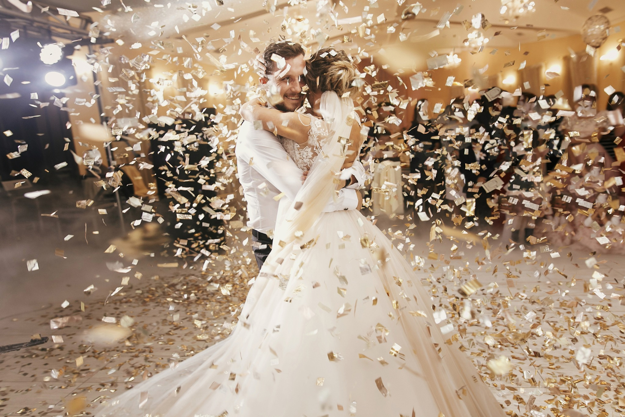 Bride and groom share a joyful first dance surrounded by golden confetti at their indoor wedding reception.
