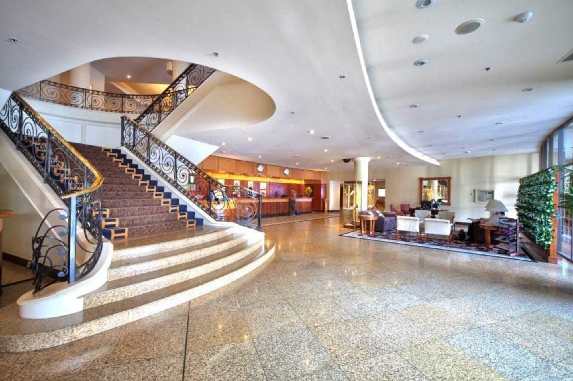 Spacious hotel lobby with a grand curved staircase and seating area, ideal for an elegant wedding venue.
