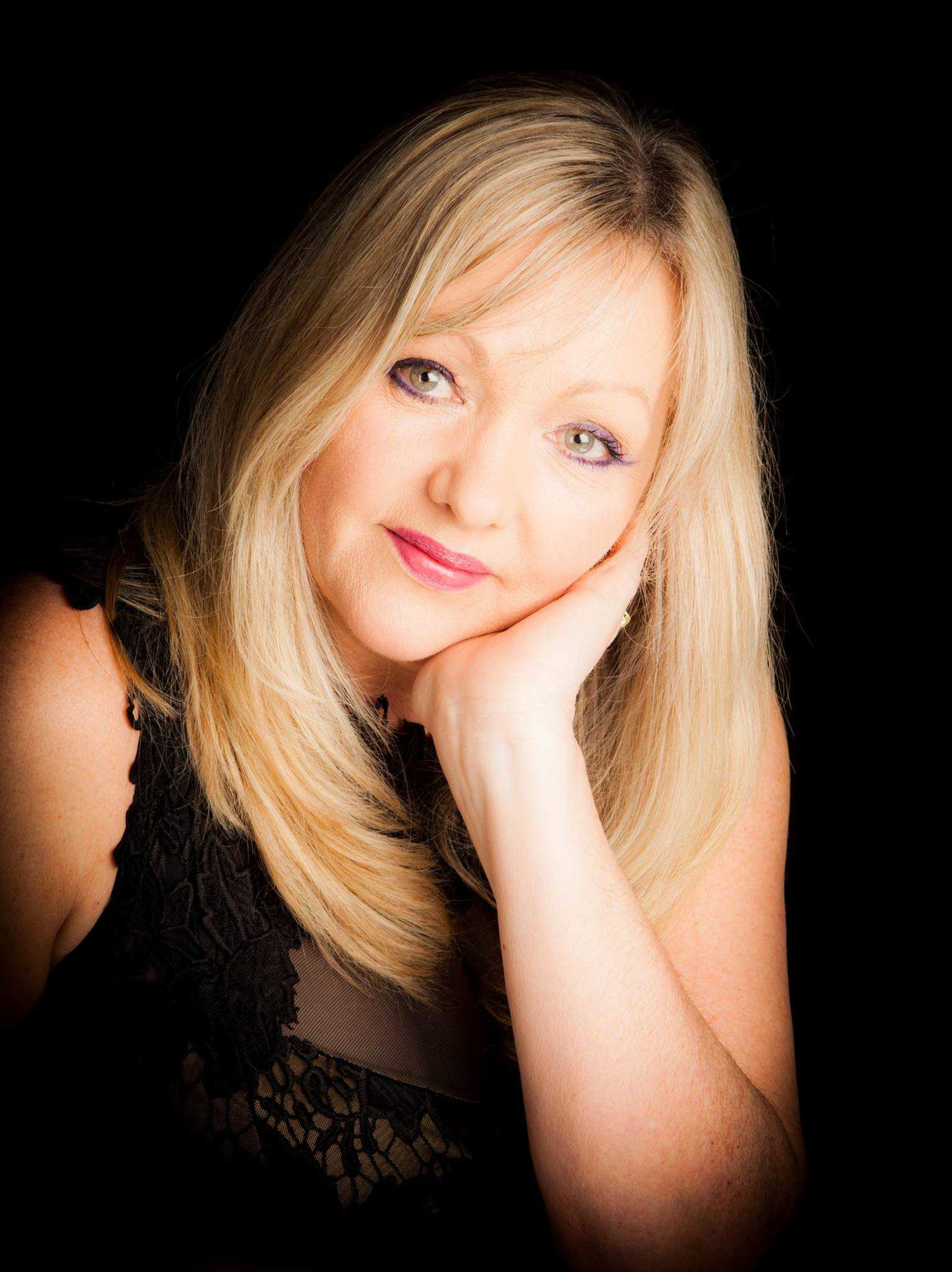 Professional portrait of a blonde woman in black lace against a dark background.