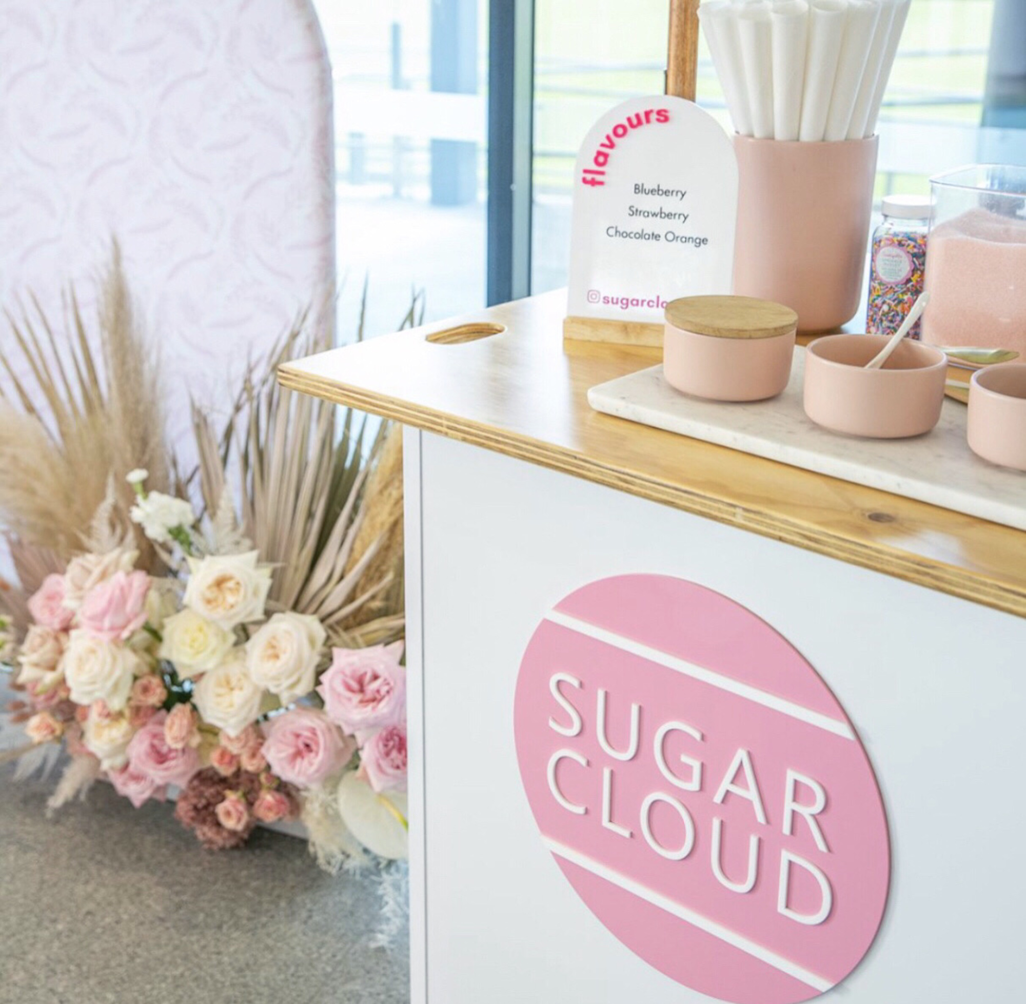 Pastel Sugar Cloud cotton candy cart with floral arrangement and wedding dessert setup.