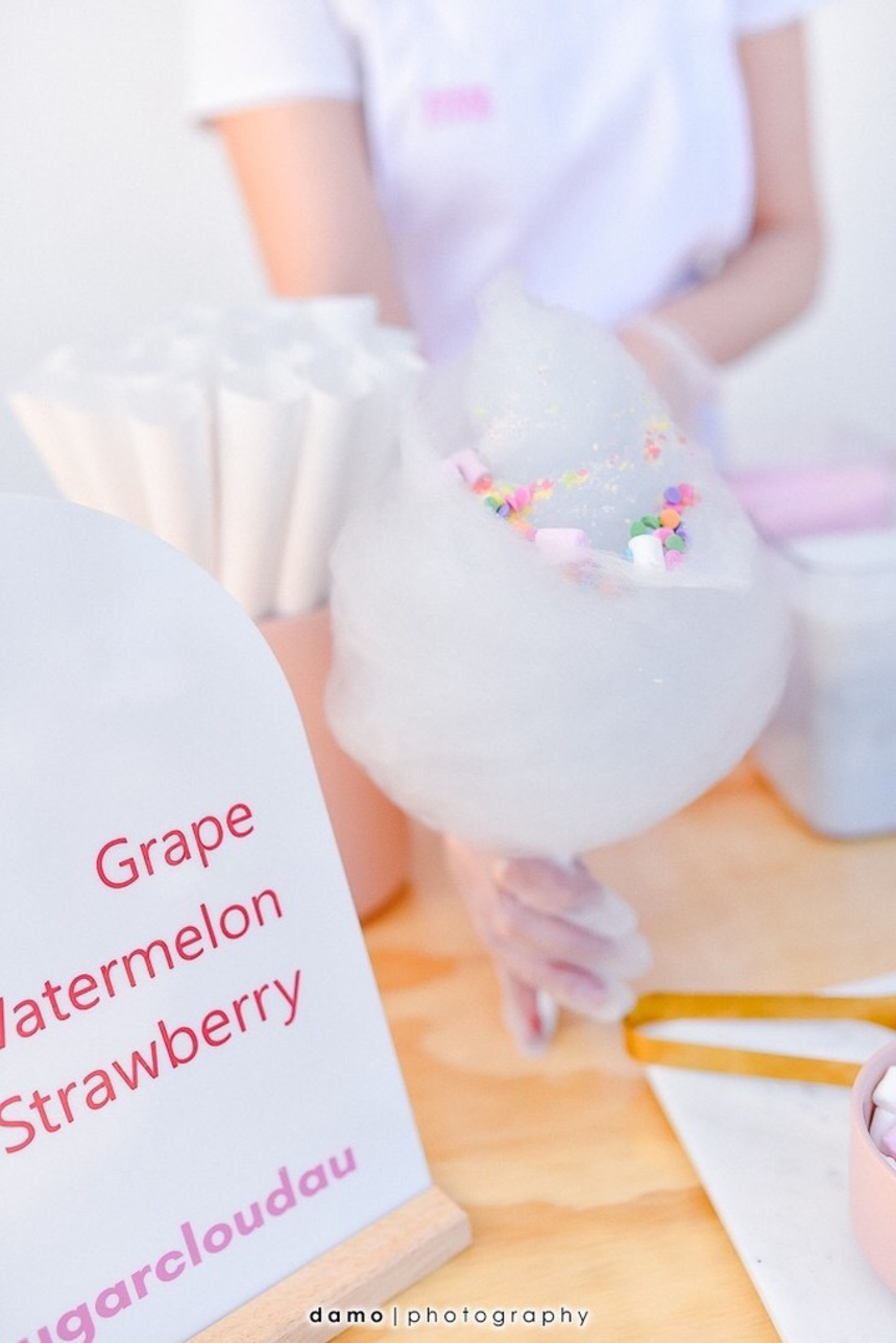 Pastel cotton candy with colorful sprinkles is served at a wedding dessert cart beside a flavor menu sign.