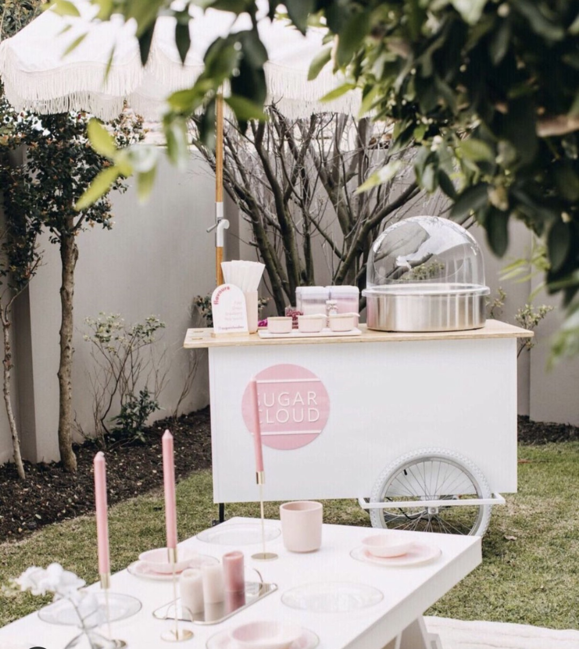 Pastel cotton candy cart and styled dessert table set up for an outdoor garden wedding reception.