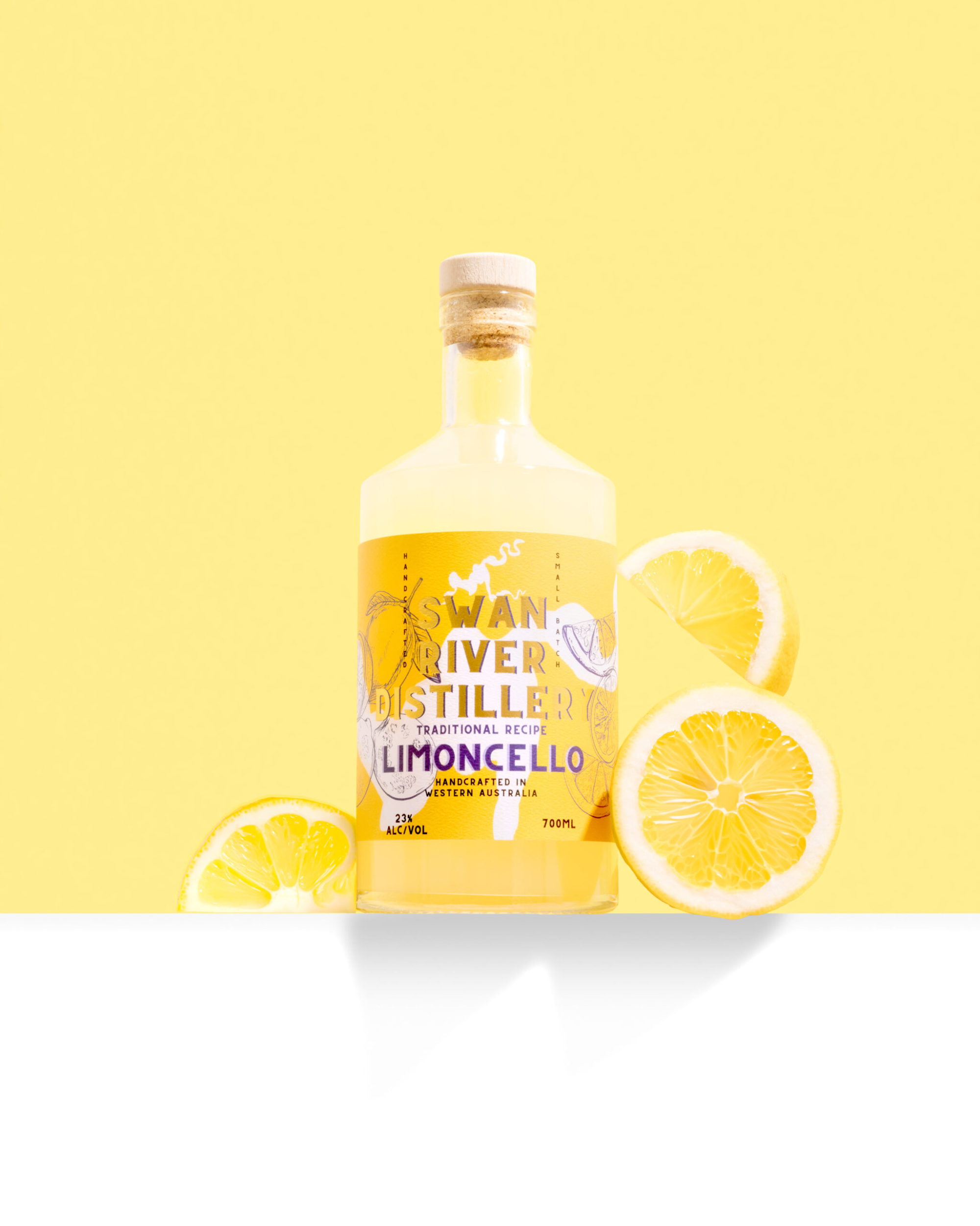 Bottle of Swan River Distillery limoncello with fresh lemon slices on a bright yellow background.