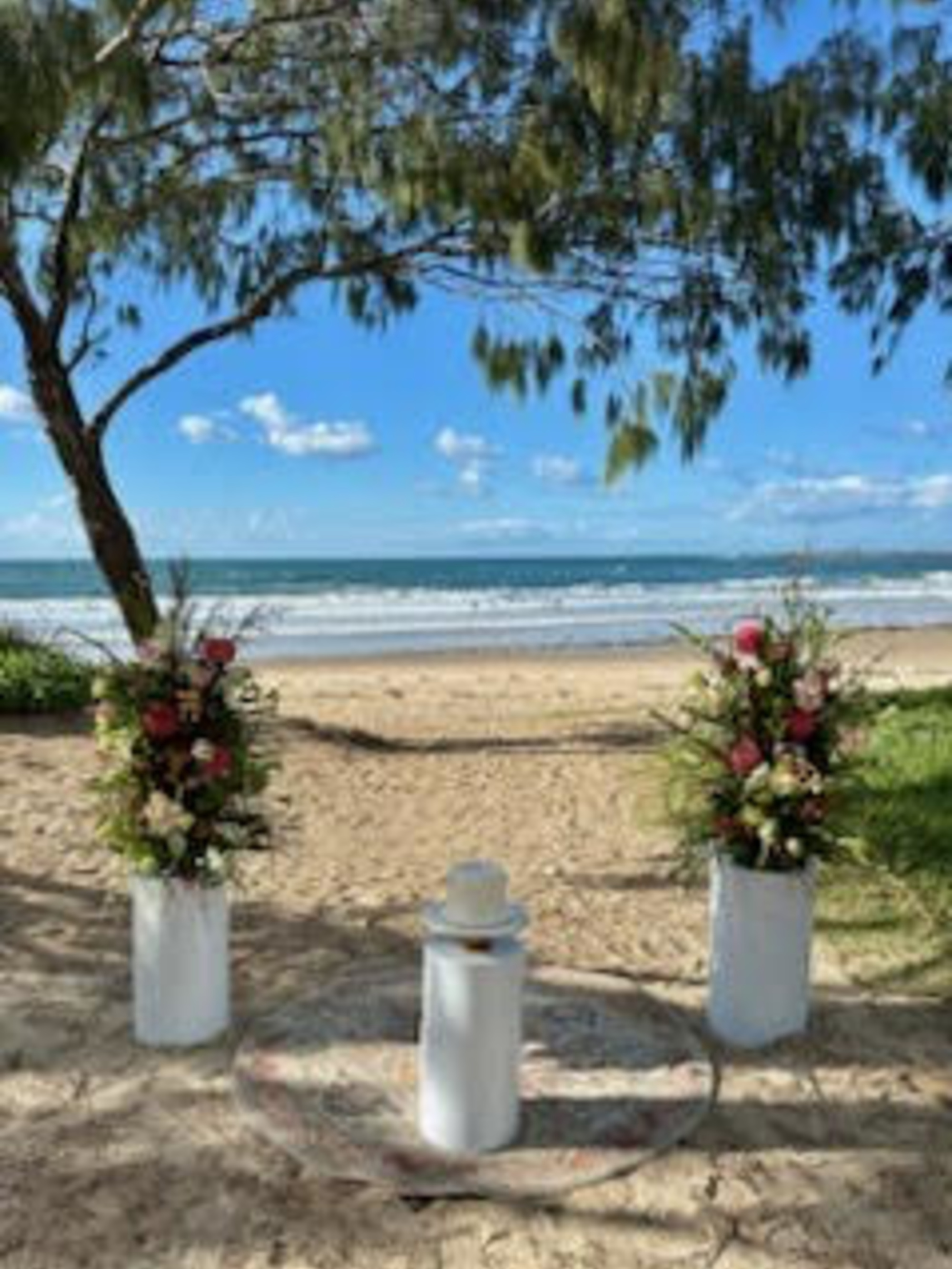 Beachfront wedding ceremony setup with floral arrangements and ocean backdrop under a sunny blue sky.