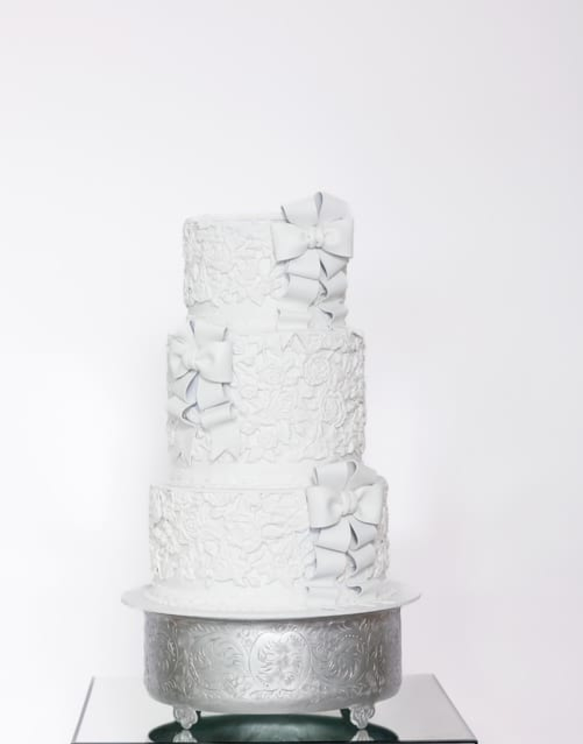 Elegant three-tier white wedding cake with lace texture and fondant bows on a silver stand