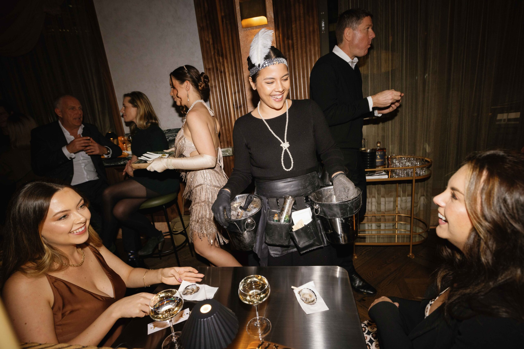 Guests enjoy oysters and drinks served by a smiling attendant at a lively indoor wedding reception.
