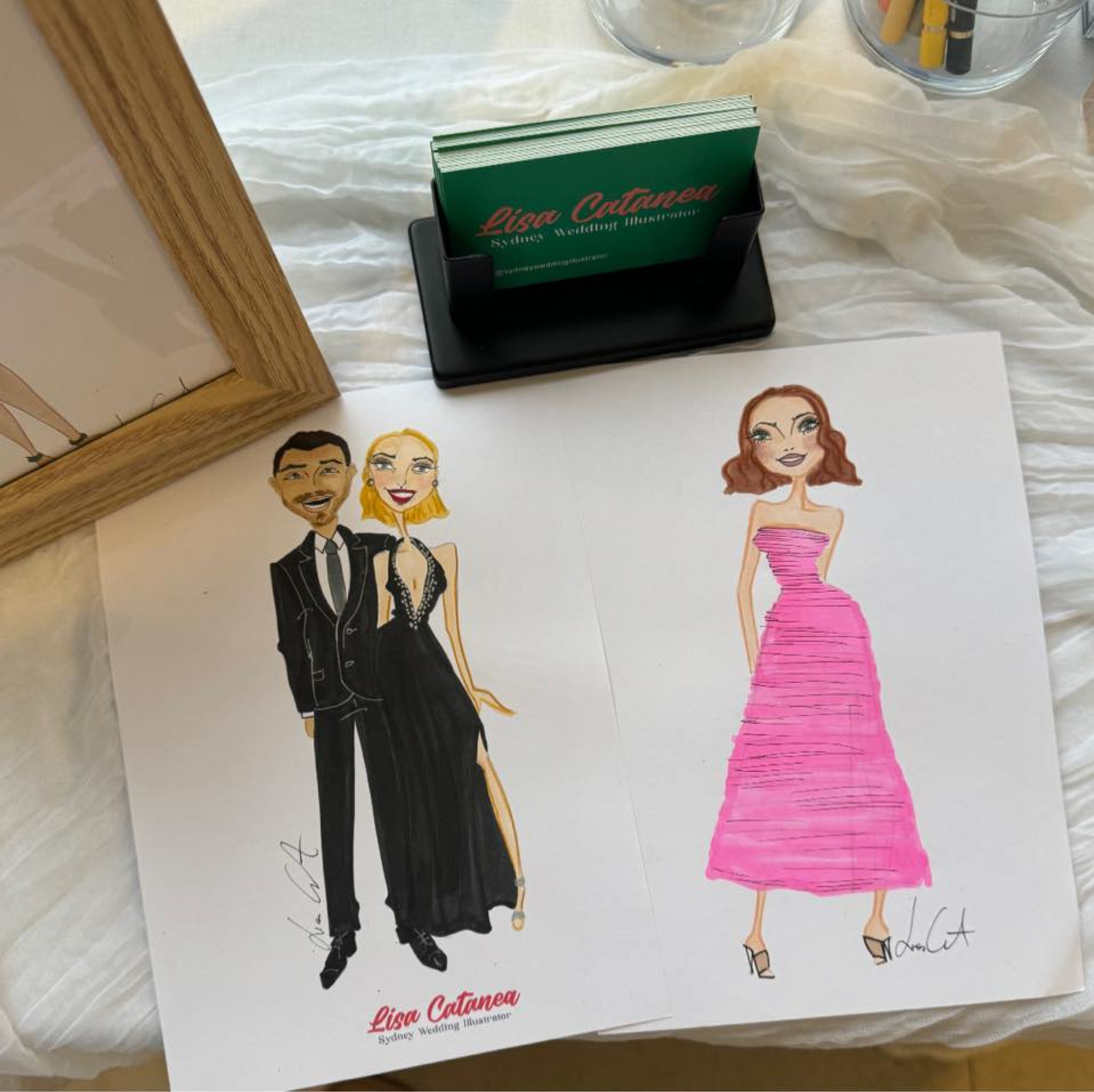 Display of colorful wedding fashion illustrations and business cards for a wedding illustrator on a white table.