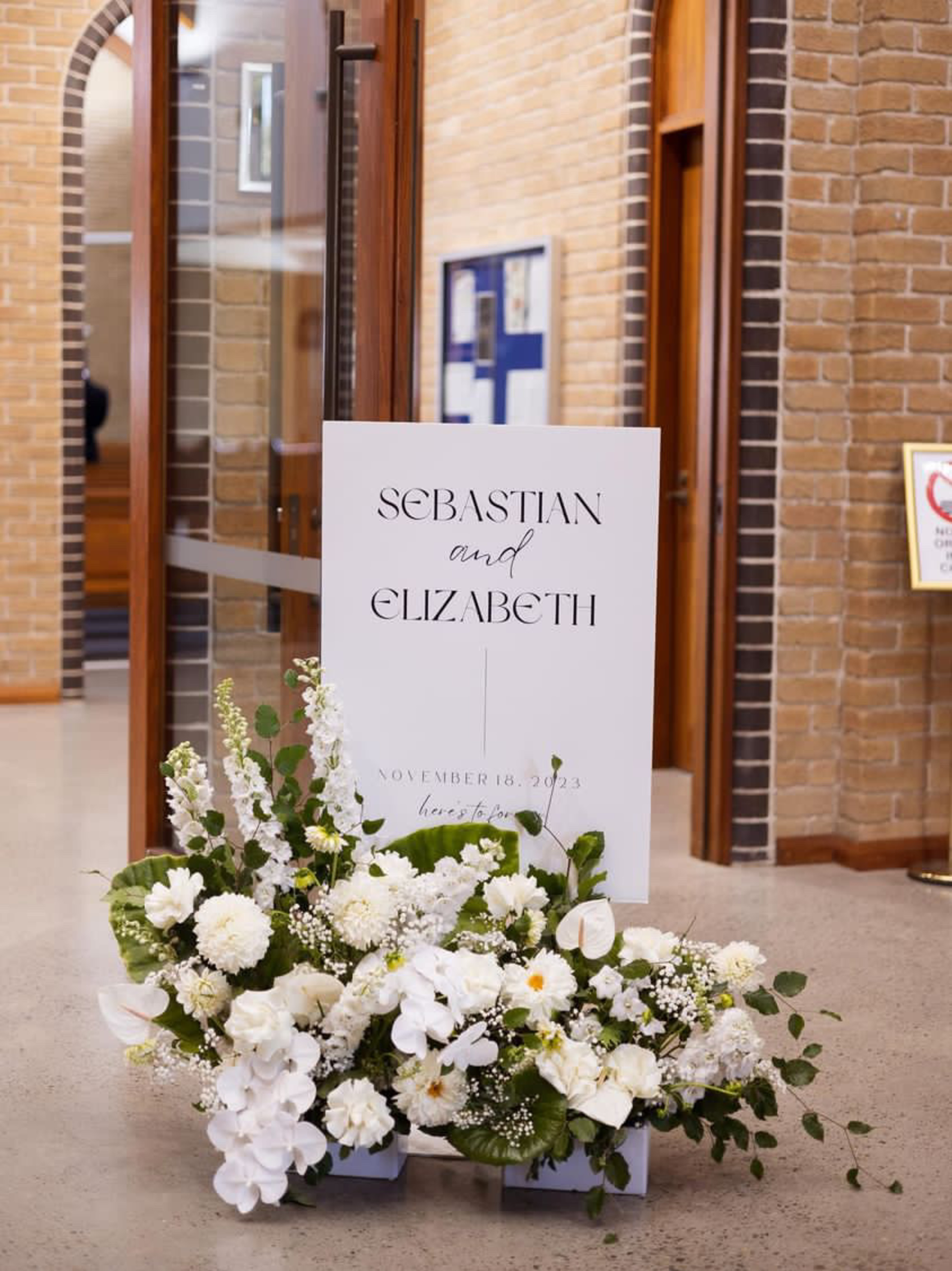 Modern wedding welcome sign with white floral arrangements at a church entrance