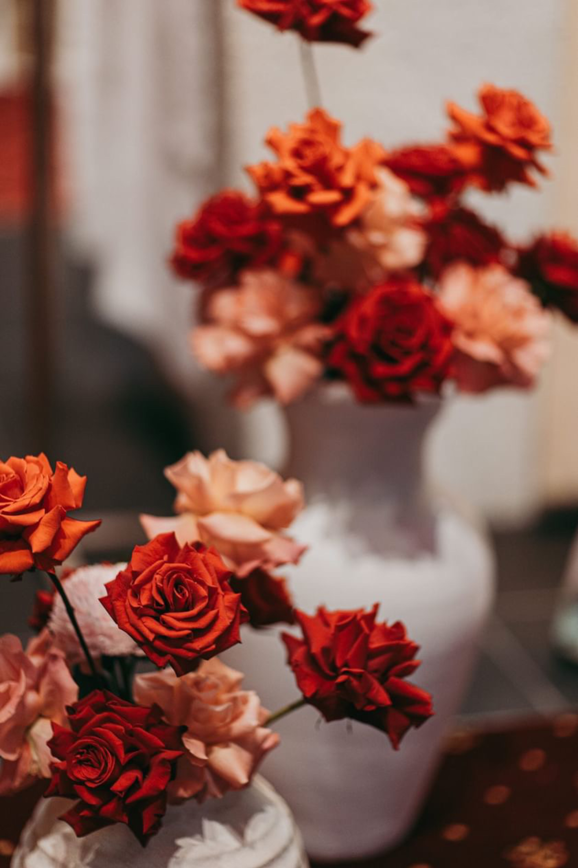 Red and blush roses arranged in white vases as romantic wedding centerpieces.