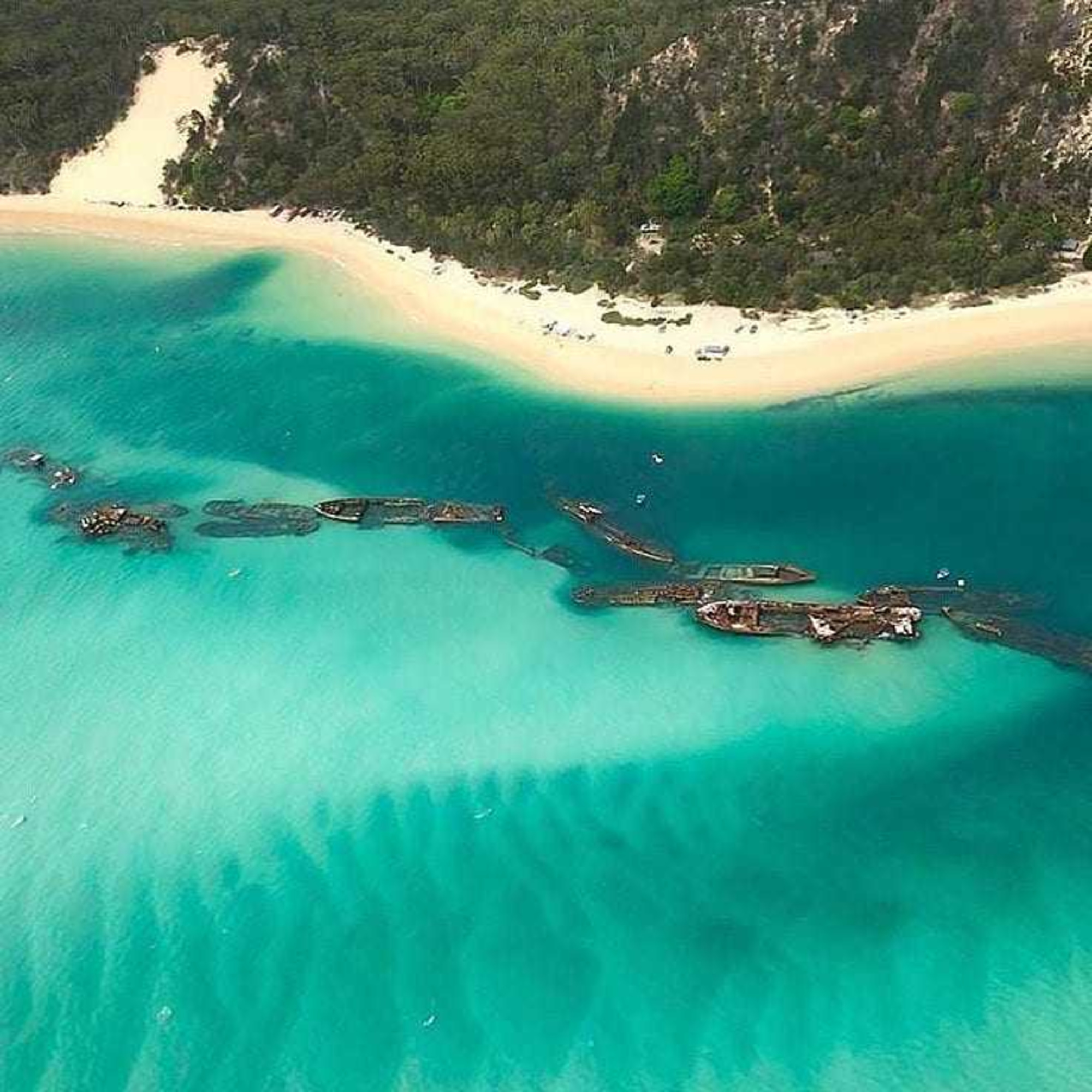 Aerial view of a tropical beach with turquoise water, shipwrecks, and lush green coastline.