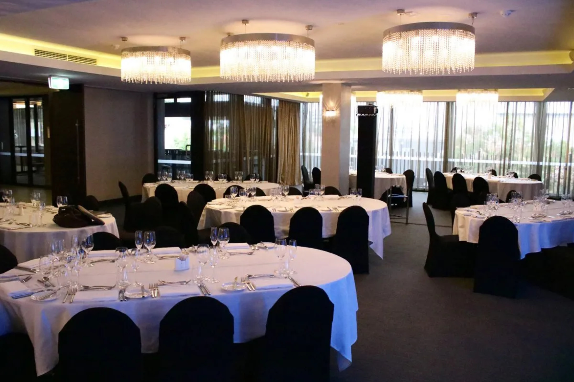 Elegant indoor wedding reception venue with round tables, black chairs, and crystal chandeliers