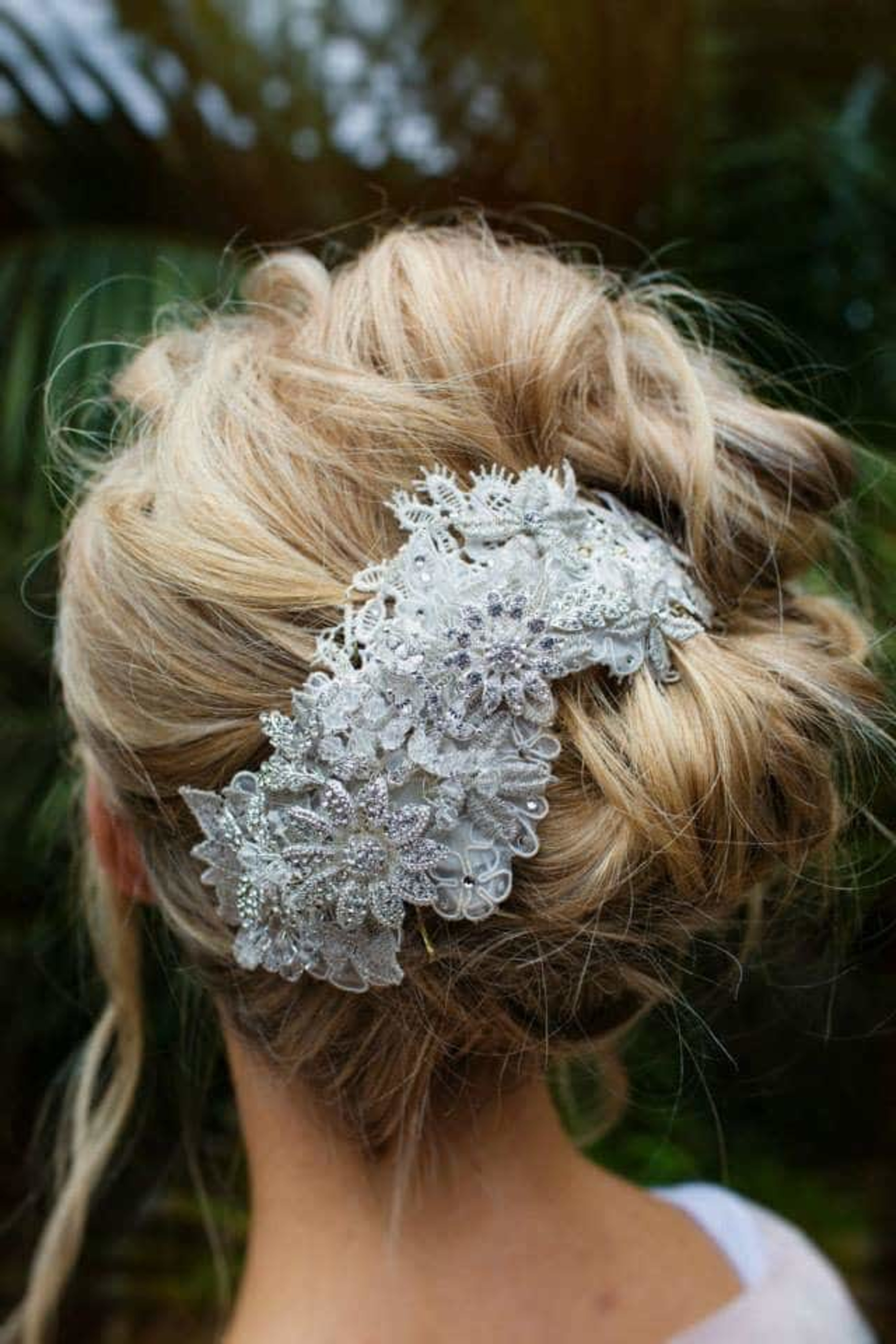Bridal updo adorned with a detailed silver floral lace hairpiece viewed from the back.