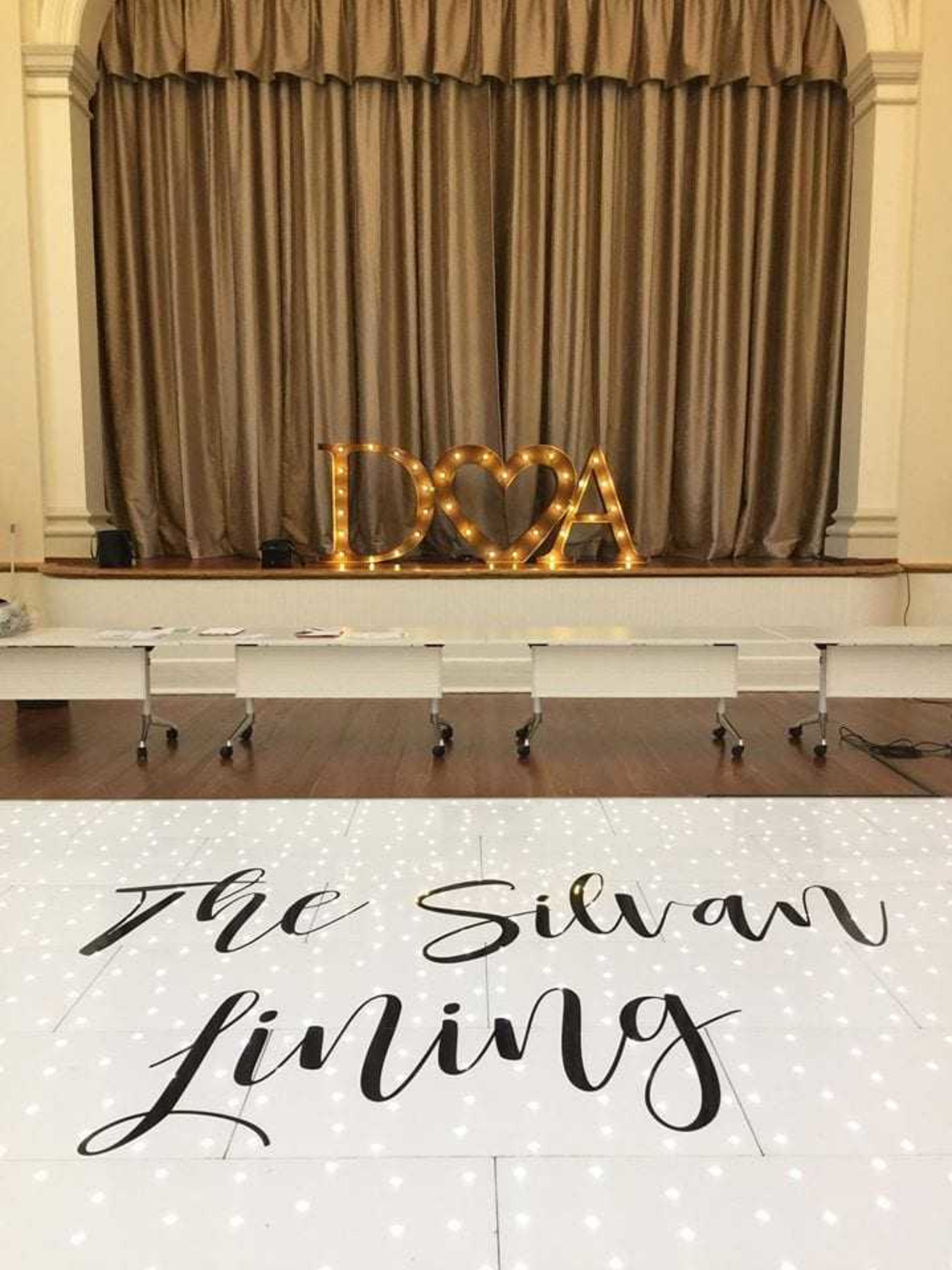 Indoor wedding stage with illuminated initials and a white sparkling dance floor reading The Silvan Lining.