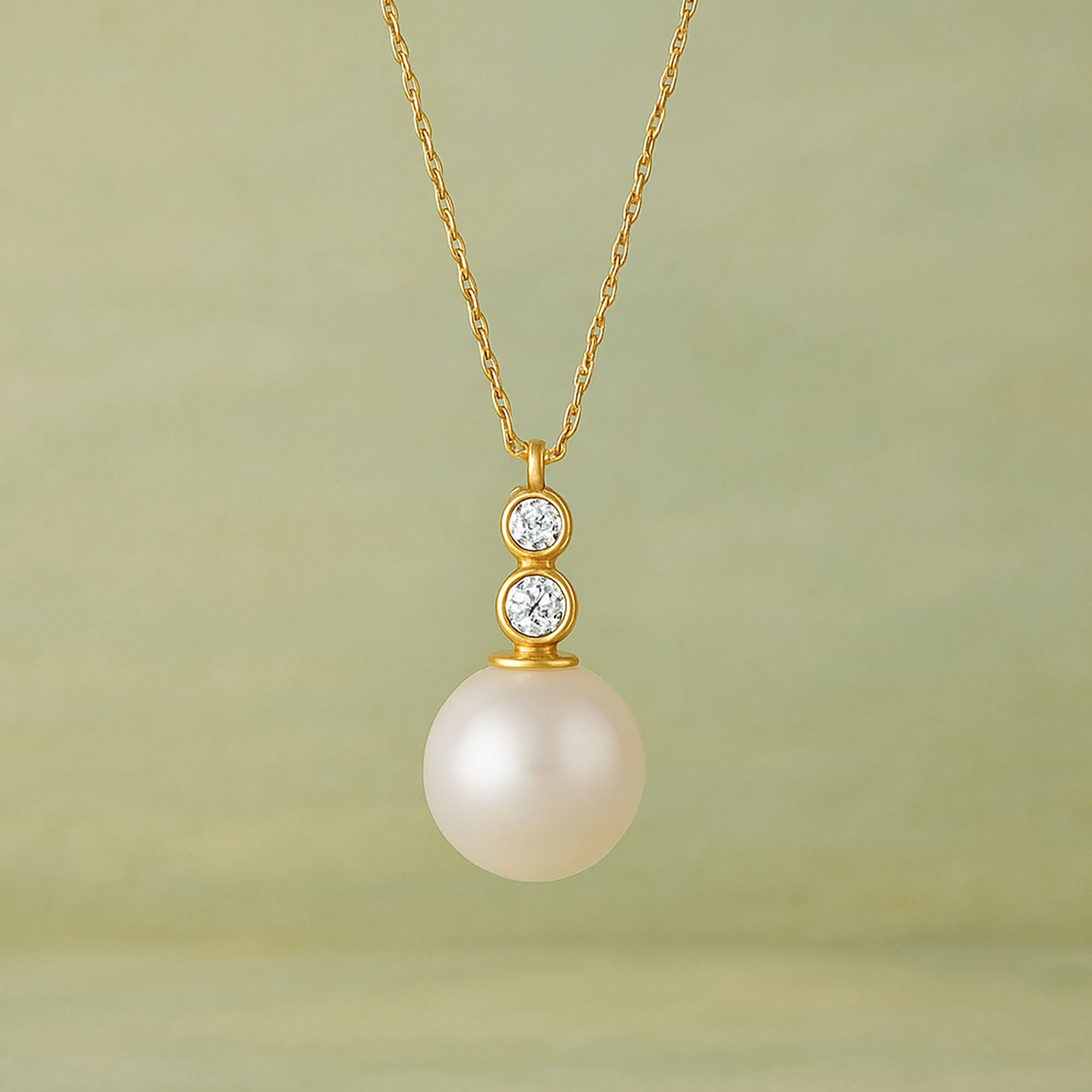 Gold chain necklace with a pearl and two diamond accents against a soft green background.