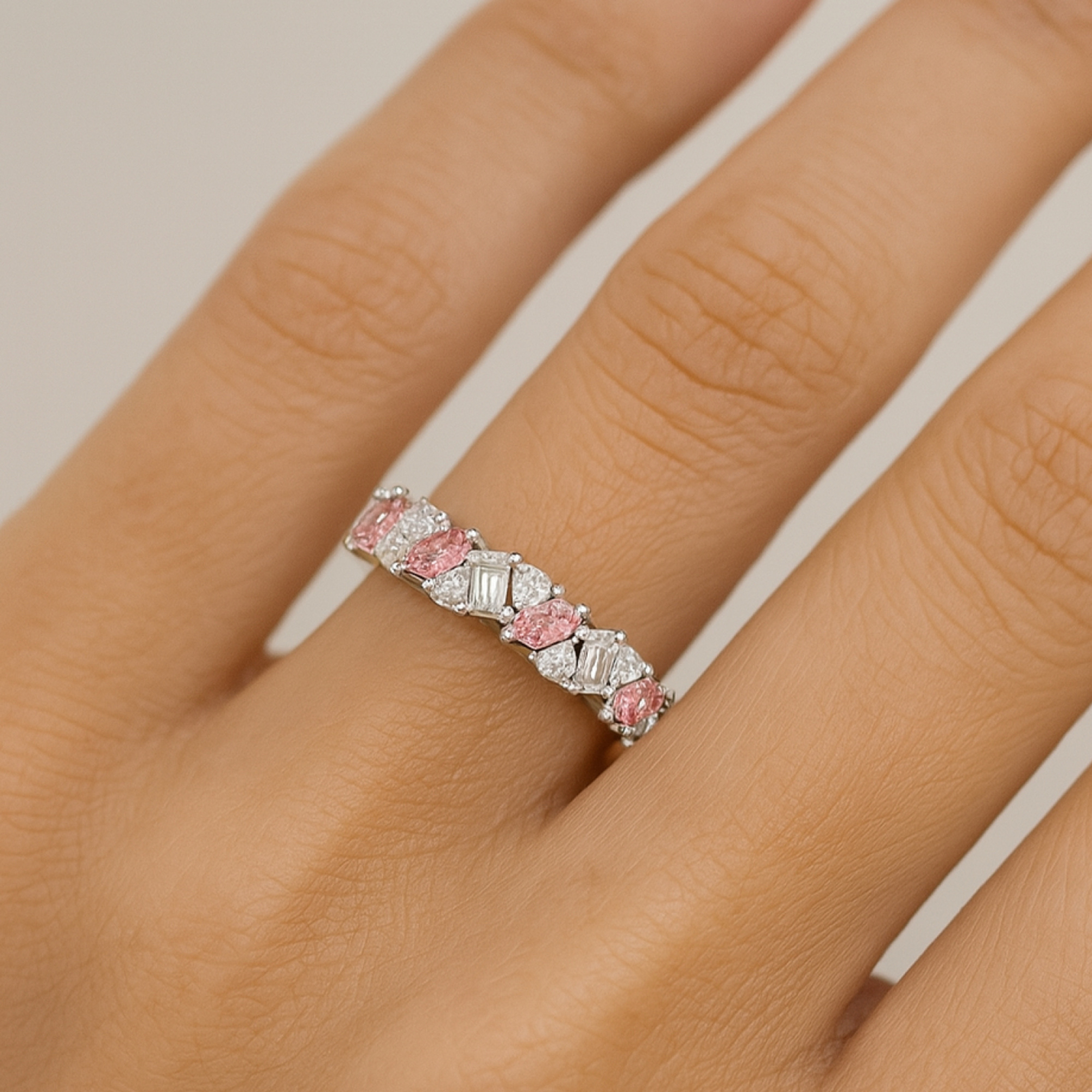 Close-up of a hand wearing a white gold eternity band with alternating pink and white gemstones.