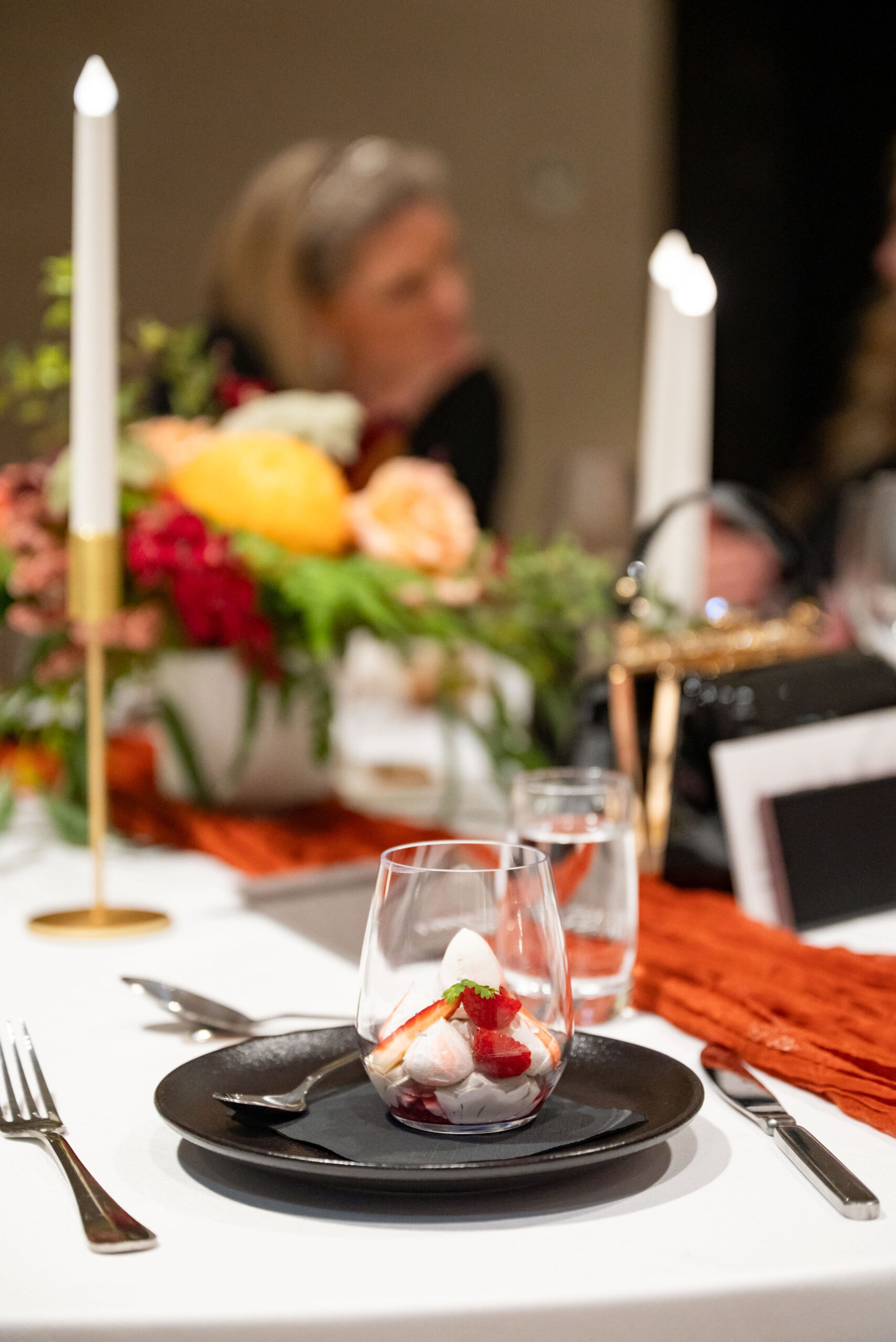 Elegant wedding table setting with a plated dessert, floral centerpiece, and tall candles.