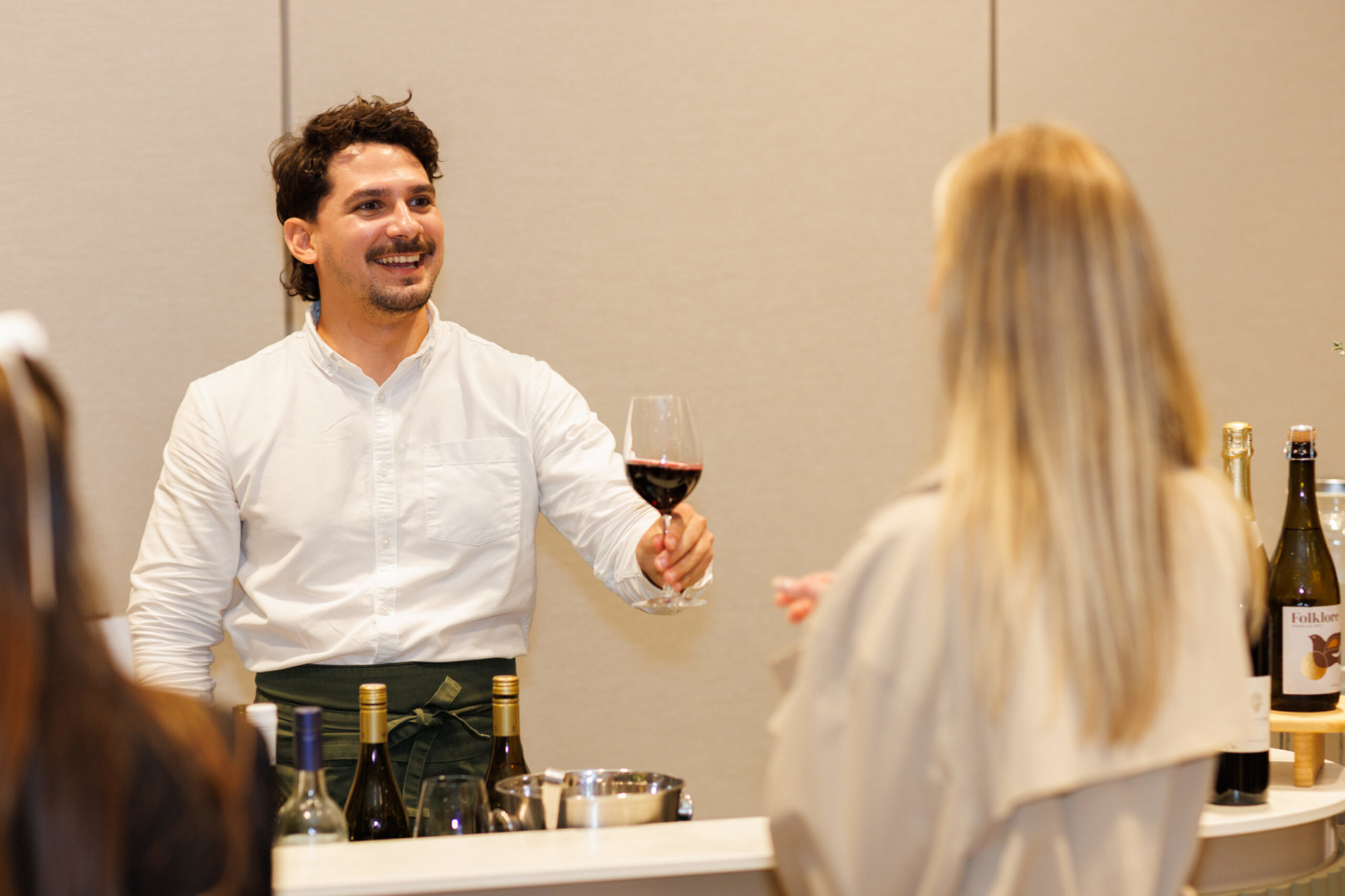 Smiling bartender serves a glass of red wine to a guest at a wedding reception bar.