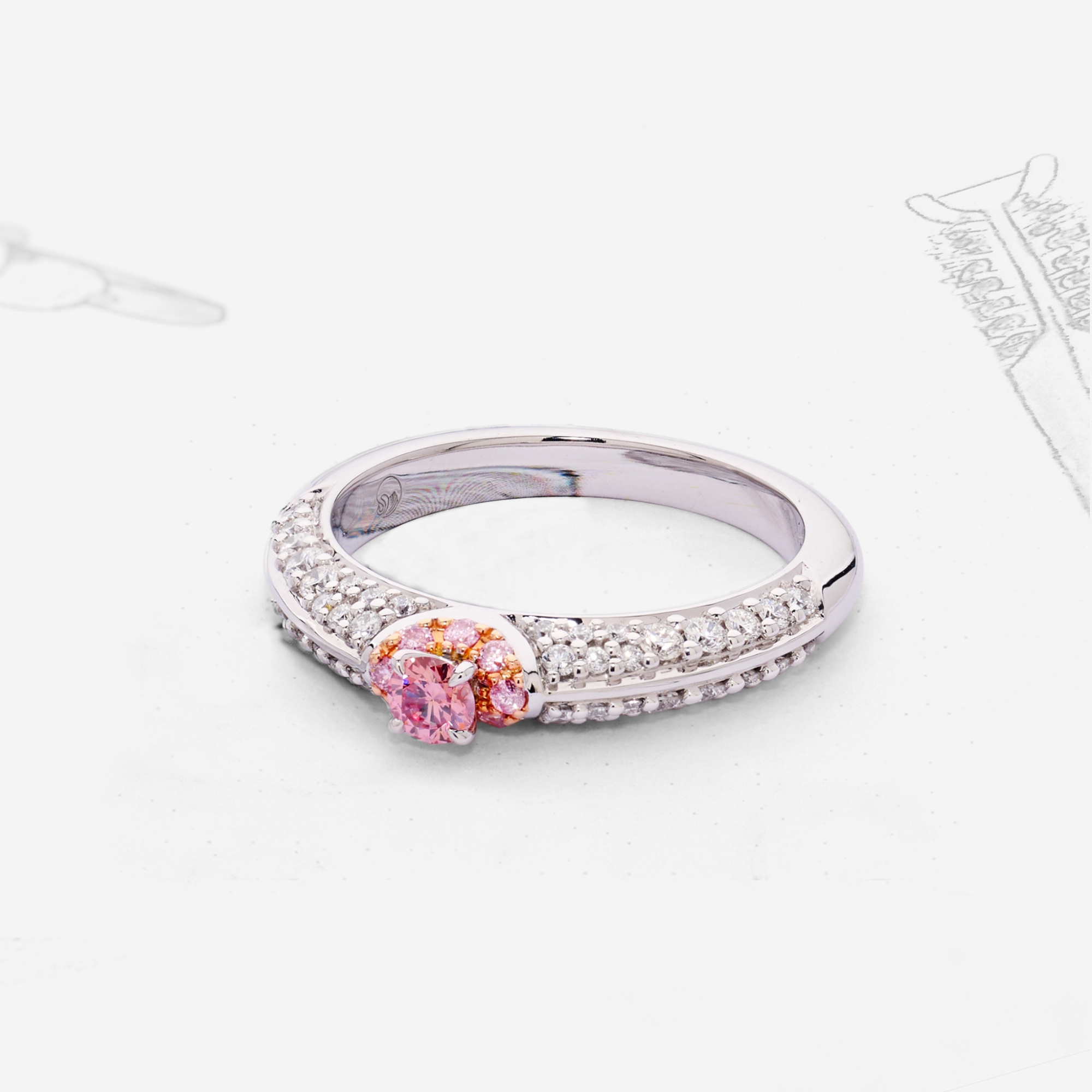 Close-up of a white gold engagement ring with pink center stone and diamond band on a light background.