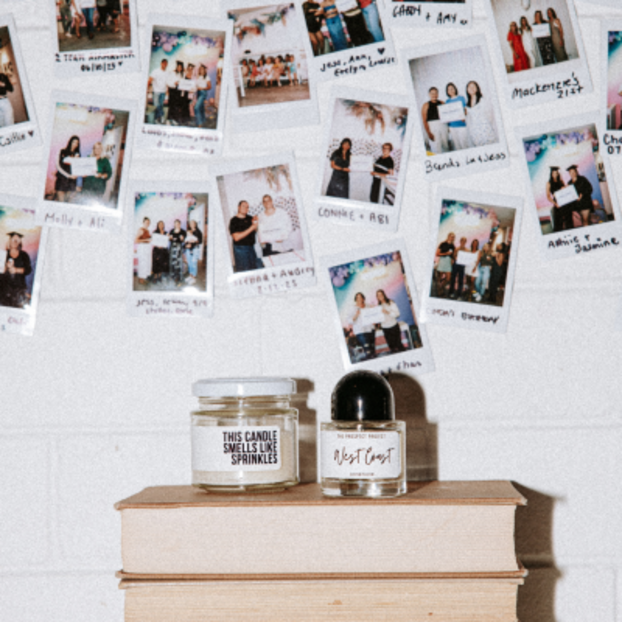 Polaroid wedding photos displayed on a wall above books with a candle and perfume bottle.