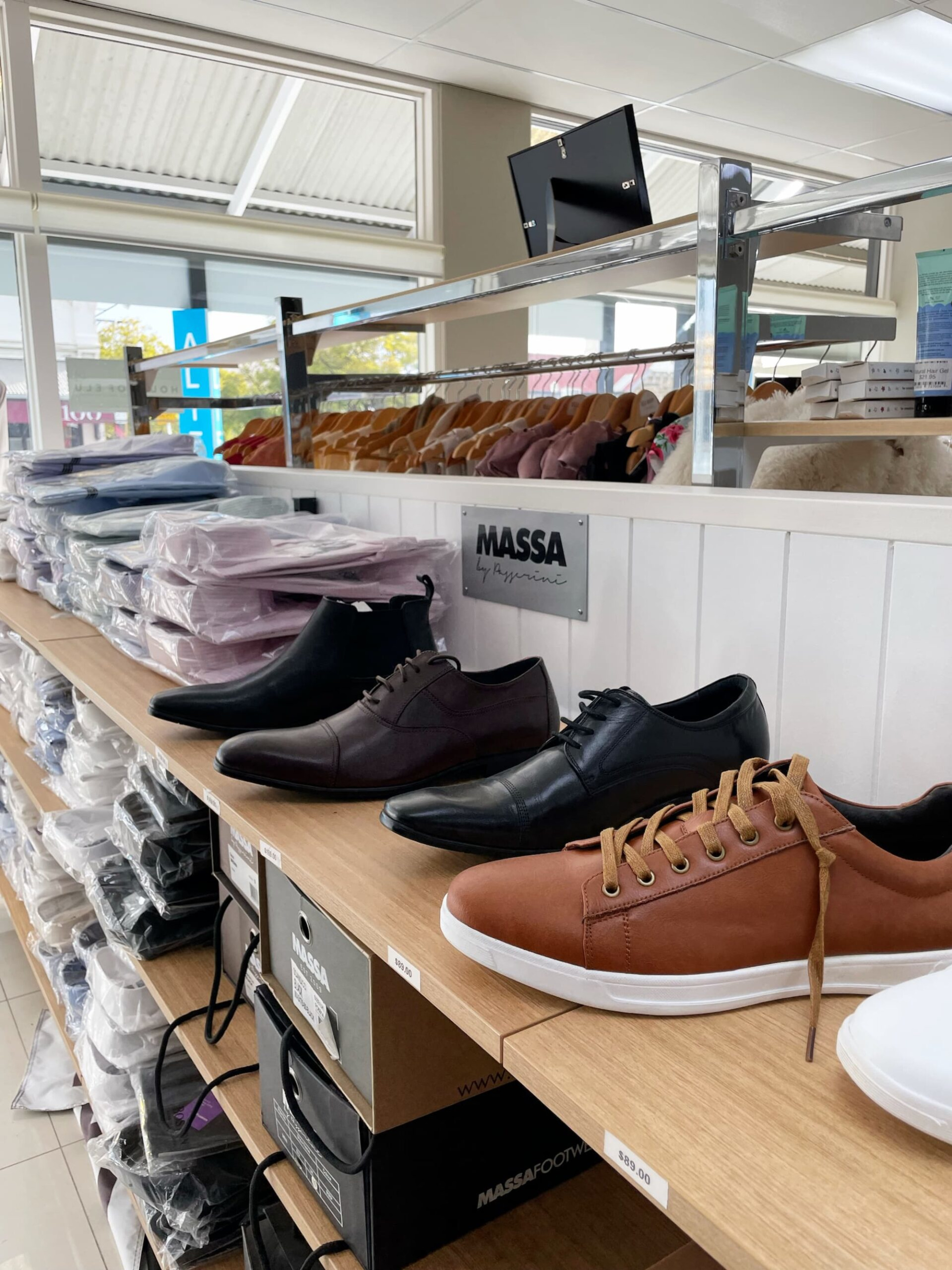 Display of men’s dress shoes and shirts in a formalwear store, suitable for grooms and groomsmen.
