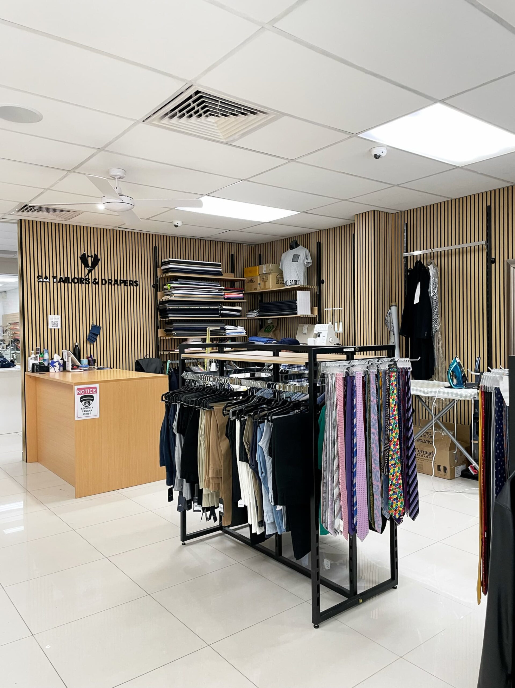 Interior of a tailor shop with racks of pants and colorful ties displayed for formalwear.