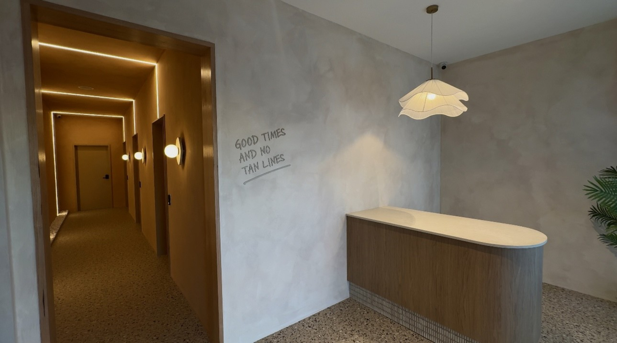Modern minimalist lobby with wood doors, terrazzo floor, and a curved reception desk under a sculptural pendant light.
