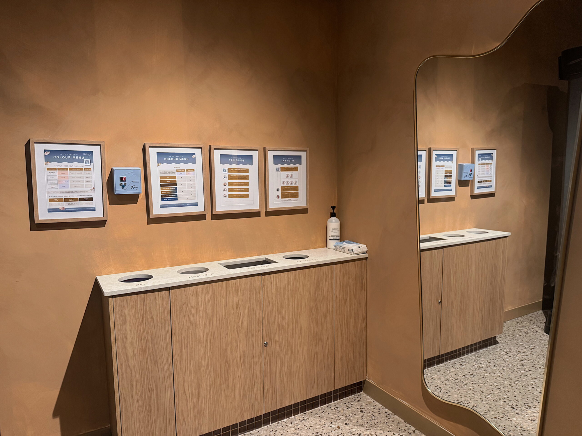 Modern venue restroom with framed wall menus, built-in countertop bins, and a large curved mirror.
