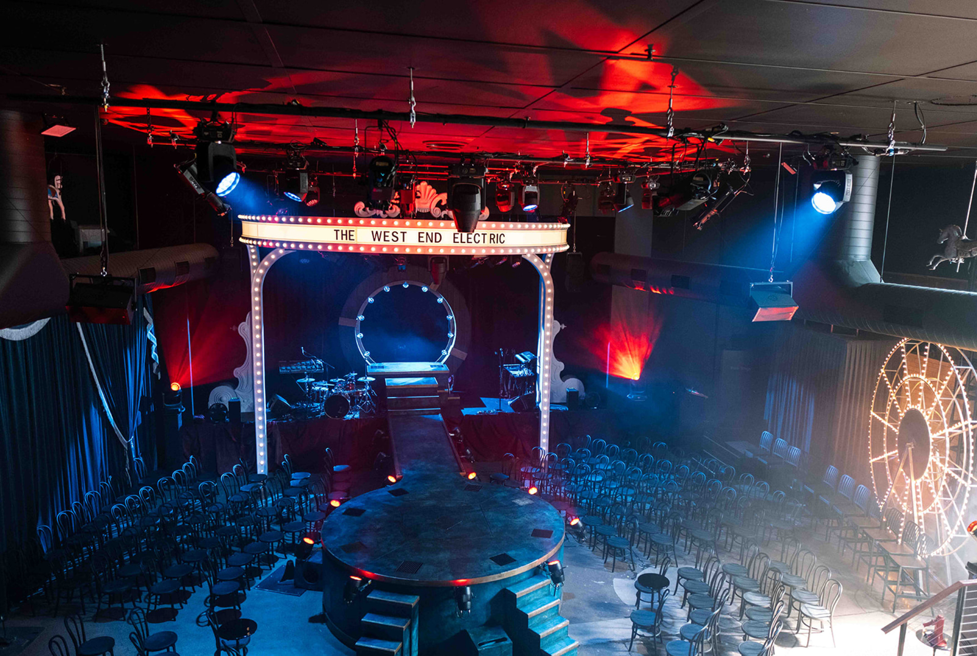 Dramatic theater-style wedding venue with circular stage, runway, and colorful concert lighting.