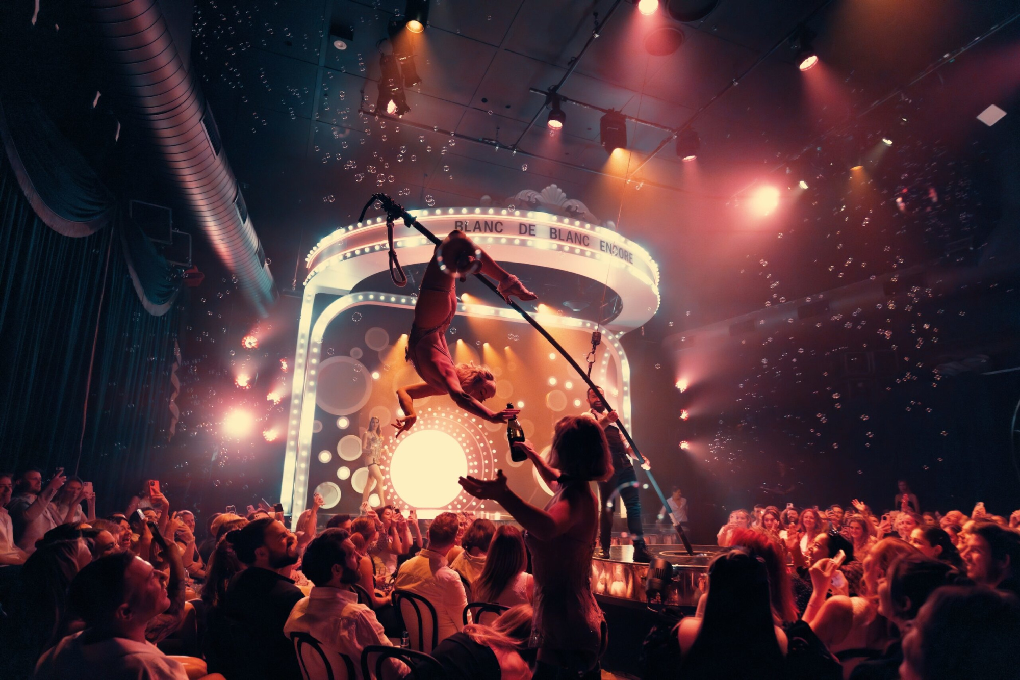 Acrobatic performers entertain guests in a vibrant cabaret-style venue with dramatic lighting and bubbles.