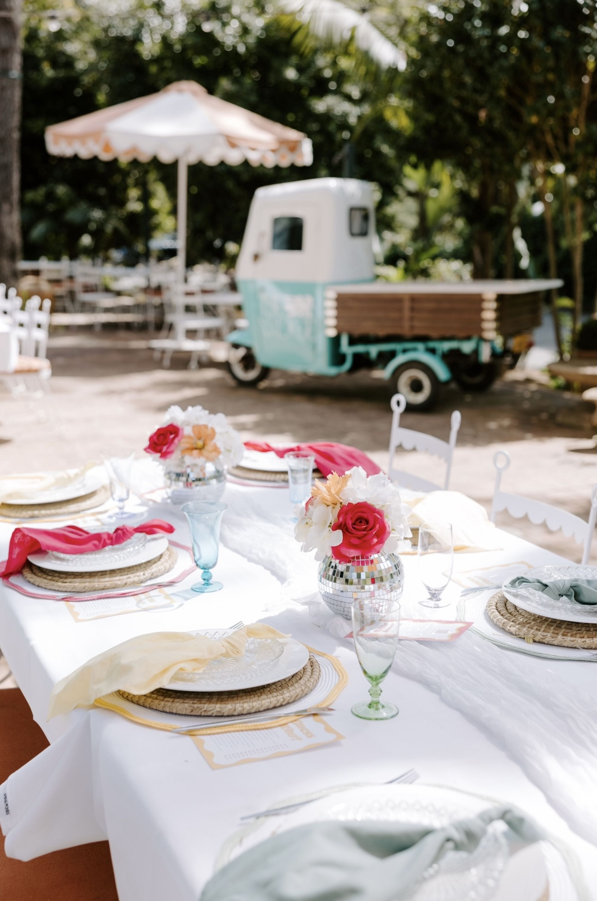 Colorful outdoor wedding reception table with disco ball floral centerpieces and a vintage turquoise truck in the background.