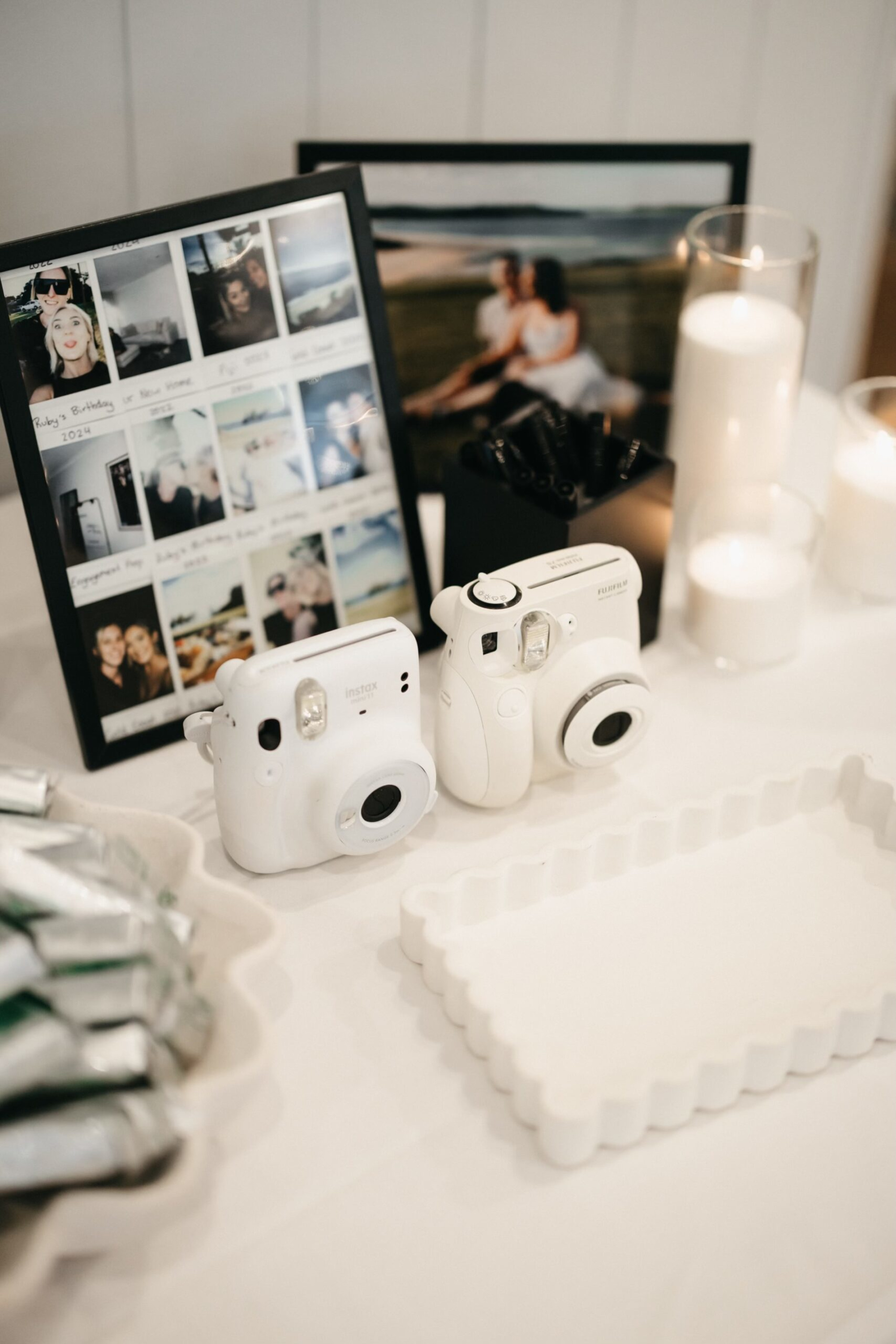 Wedding reception memory table with instant cameras, framed photos, and glowing candles arranged on a white surface.