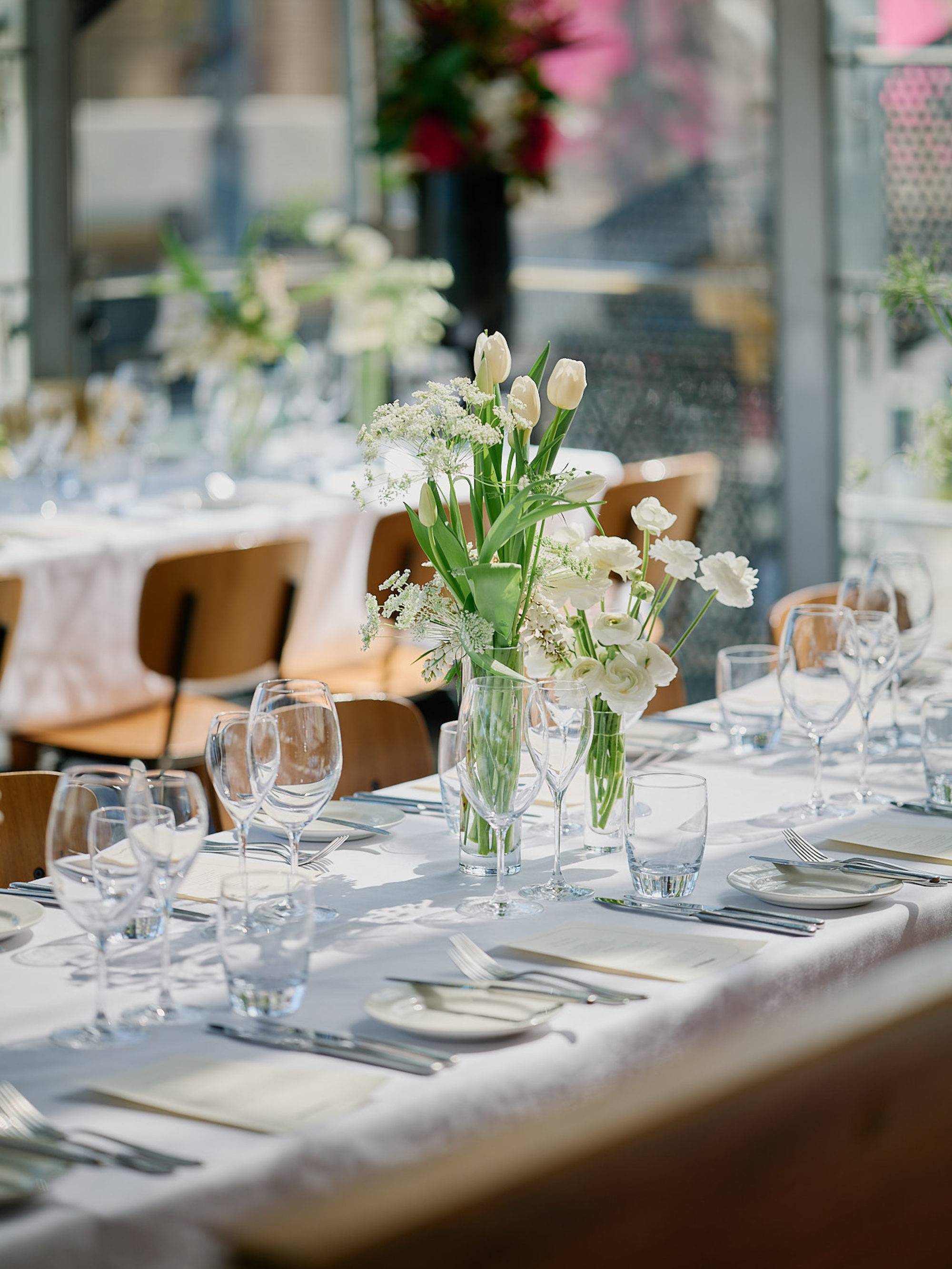 Sunlit wedding reception table set with white floral centerpieces, glassware, and neatly arranged place settings.