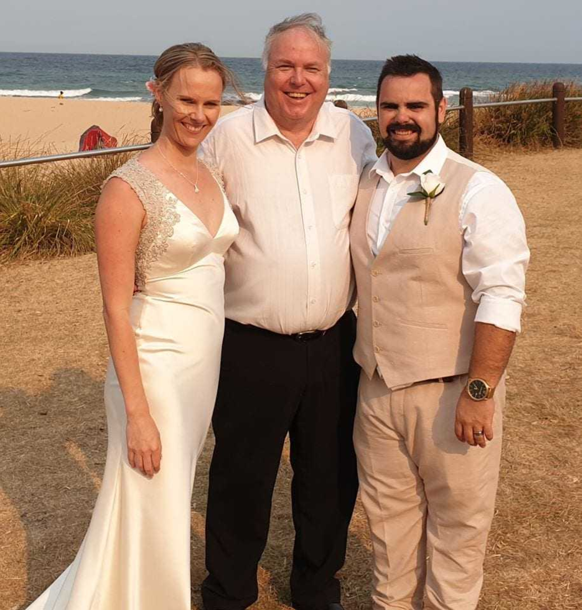 Bride, groom, and celebrant posing together at a relaxed beachside wedding ceremony.