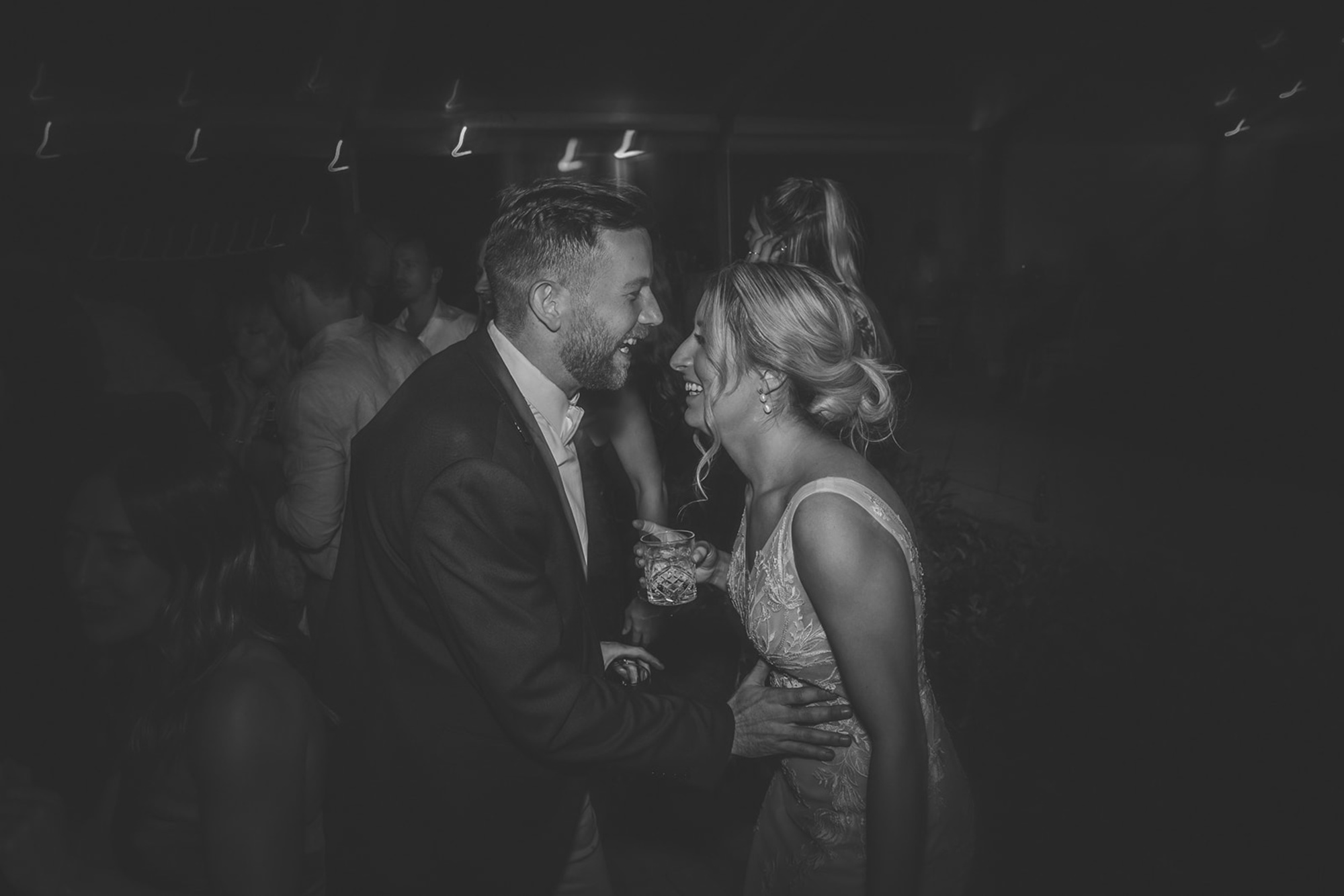 Candid black and white photo of a bride and groom laughing together on the dance floor at their wedding reception.
