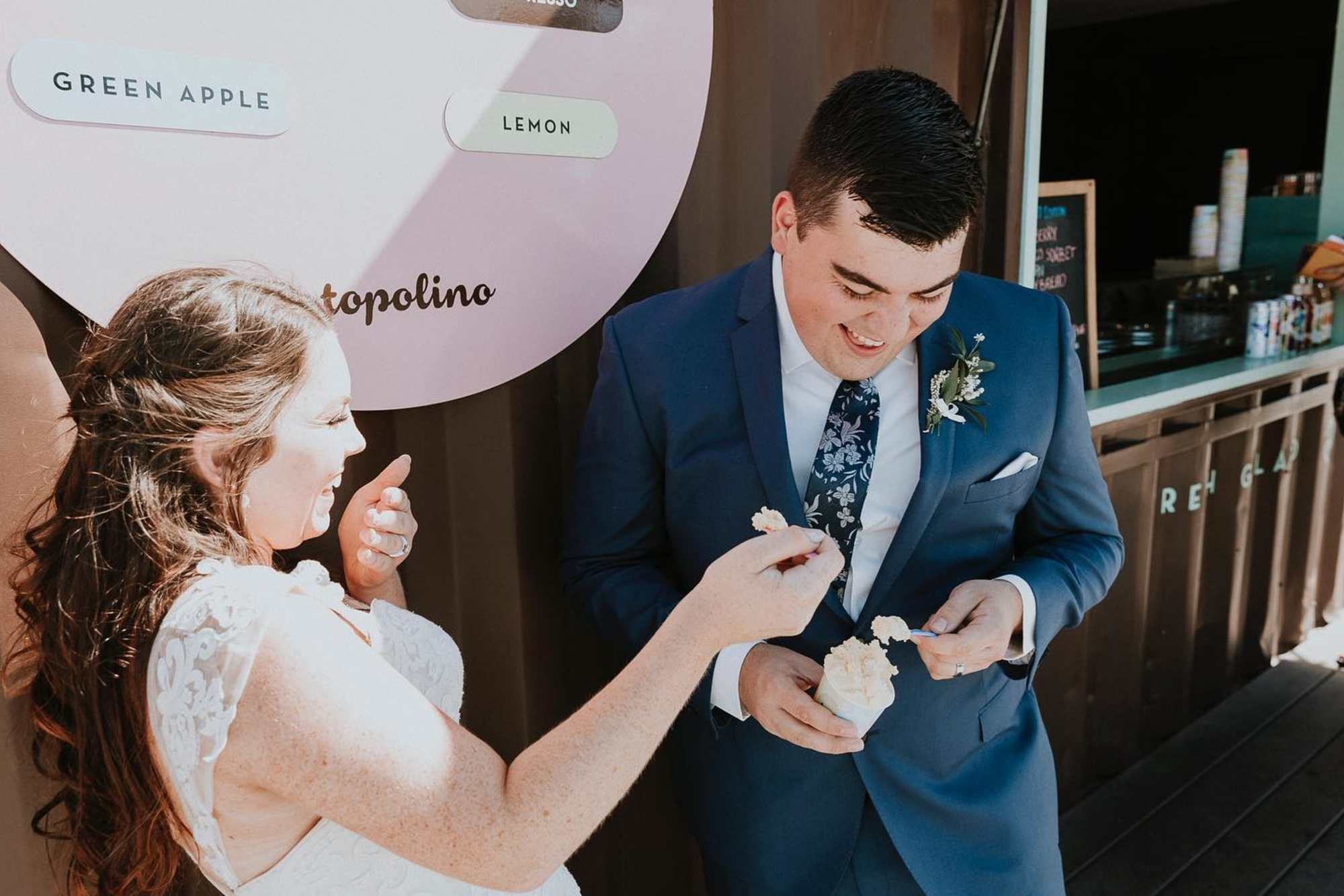 Bride and groom share a playful ice cream moment at an outdoor wedding dessert cart.